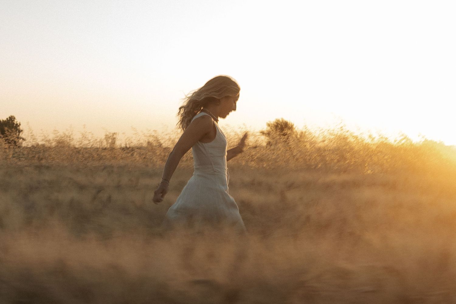 shooting photo dans un champ de blé avec une femme qui cours habillée d'une robe beige