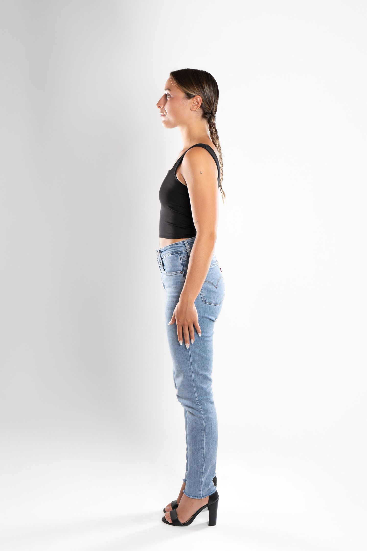 shooting photo studio en fond blanc avec une femme de profil portant un jean bleu et un top noir
