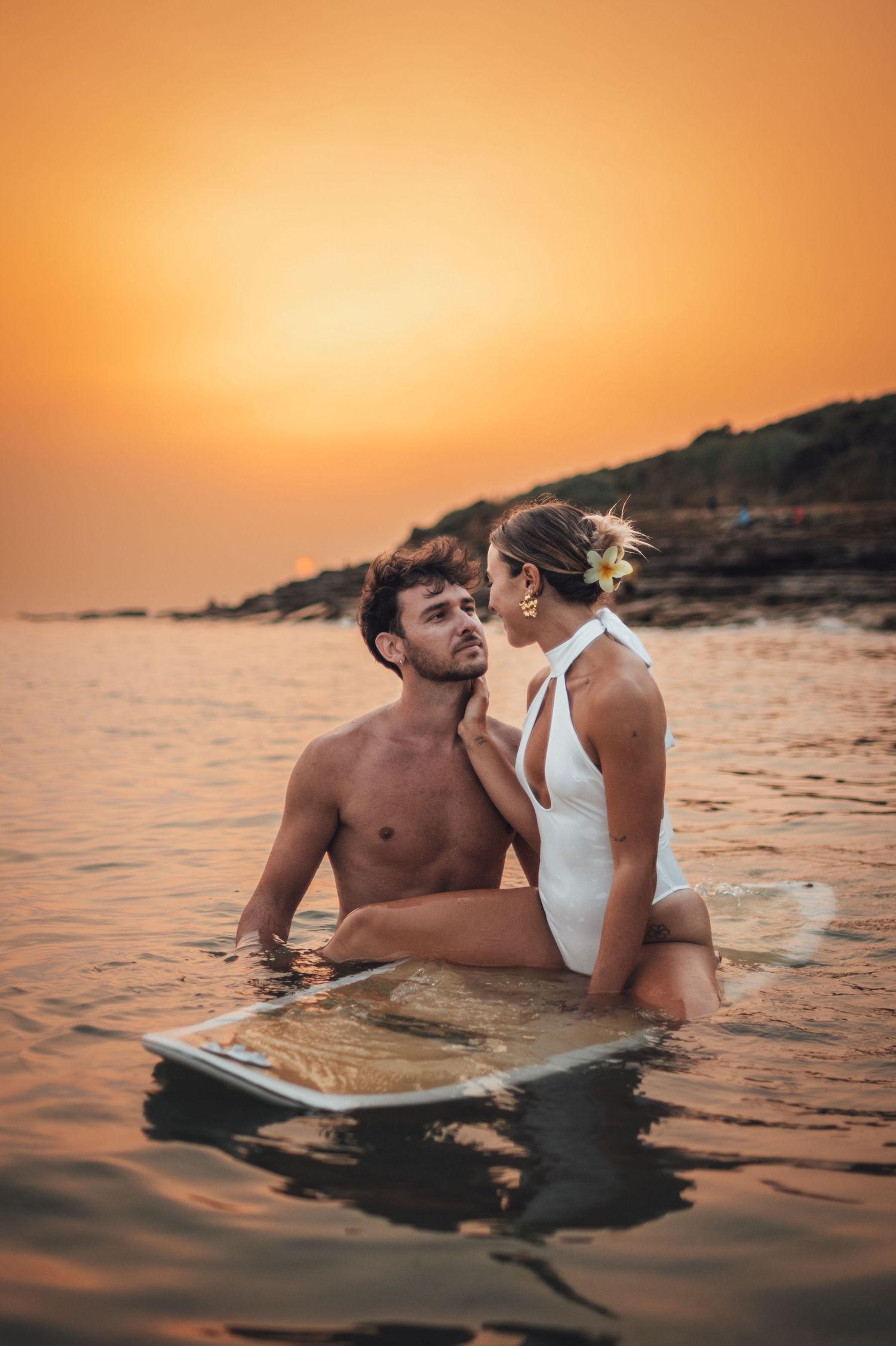 shooting photo d'un couple dans l'eau en couché de soleil orange à la plage