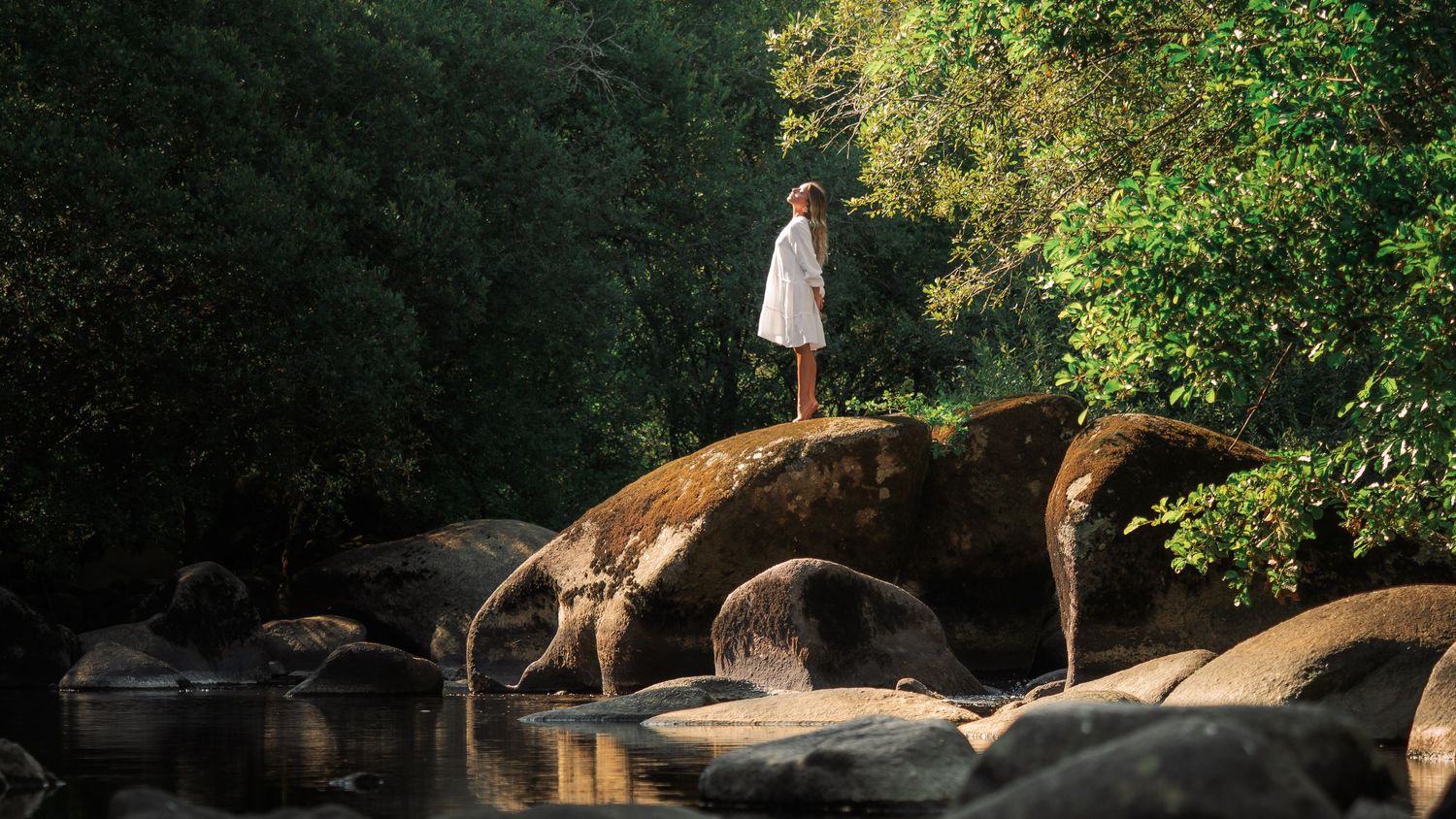shooting photo au bord d'un lac avec une femme en robe blanche sur un gros rocher