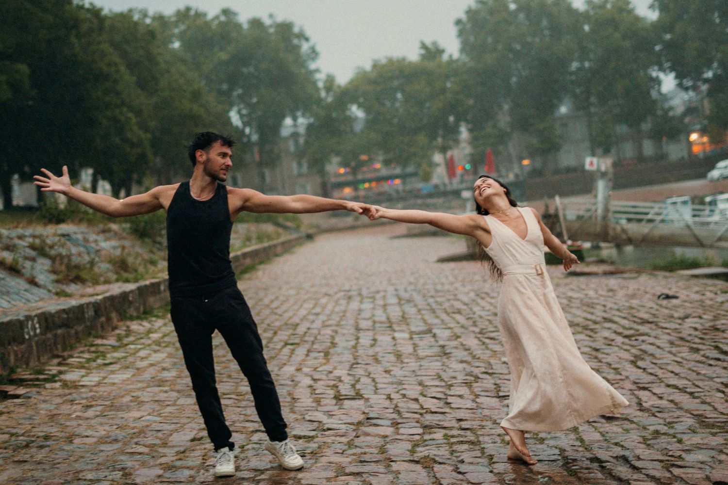couple qui danse sur le port d'Agers lors d'un shooting photo, on peut apercevoir un homme en vêtements noir et d'une femme en robe beige
