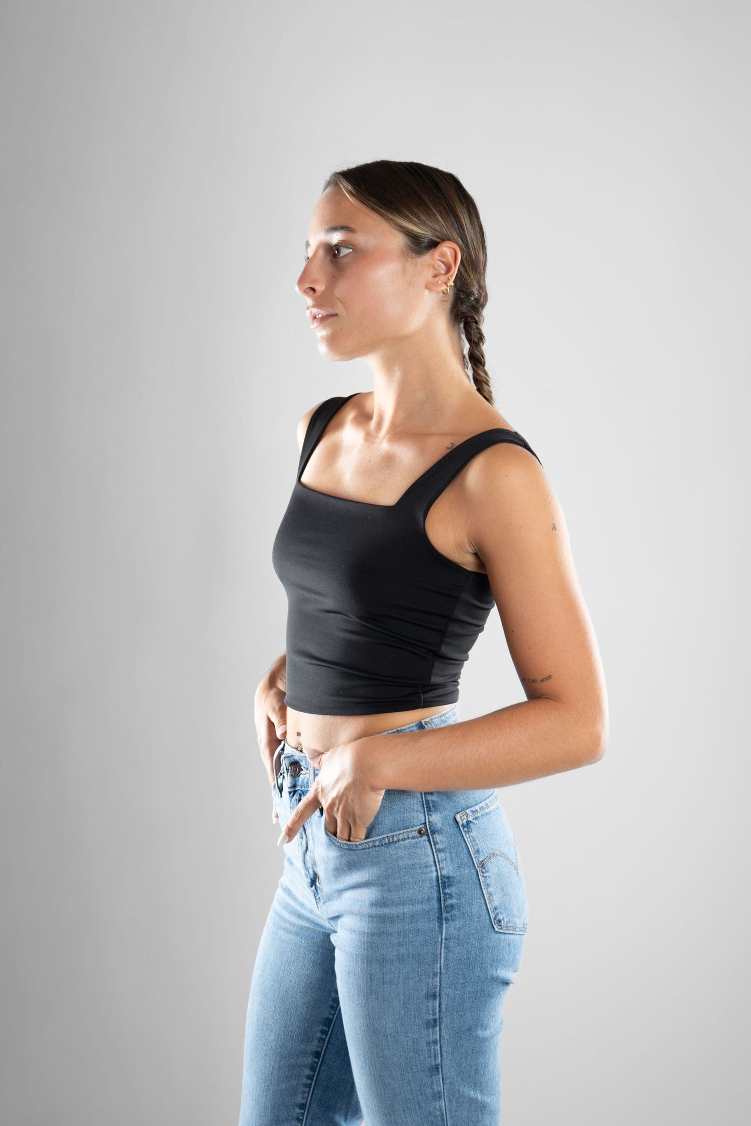 shooting photo studio en fond blanc avec une femme de profil portant un jean bleu et un top noir