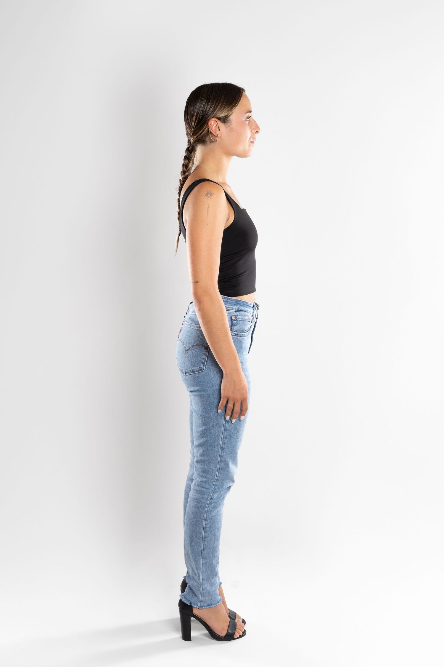 shooting photo studio en fond blanc avec une femme de profil portant un jean bleu et un top noir