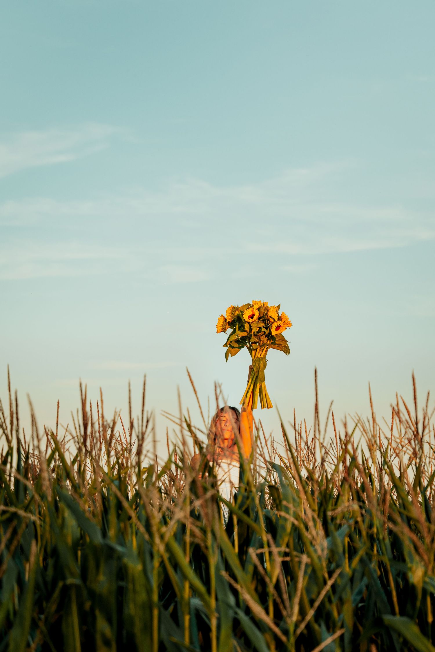 shooting photo dans un champ de mais avec une femme portant un bouquet de tournesol en tant que trophé