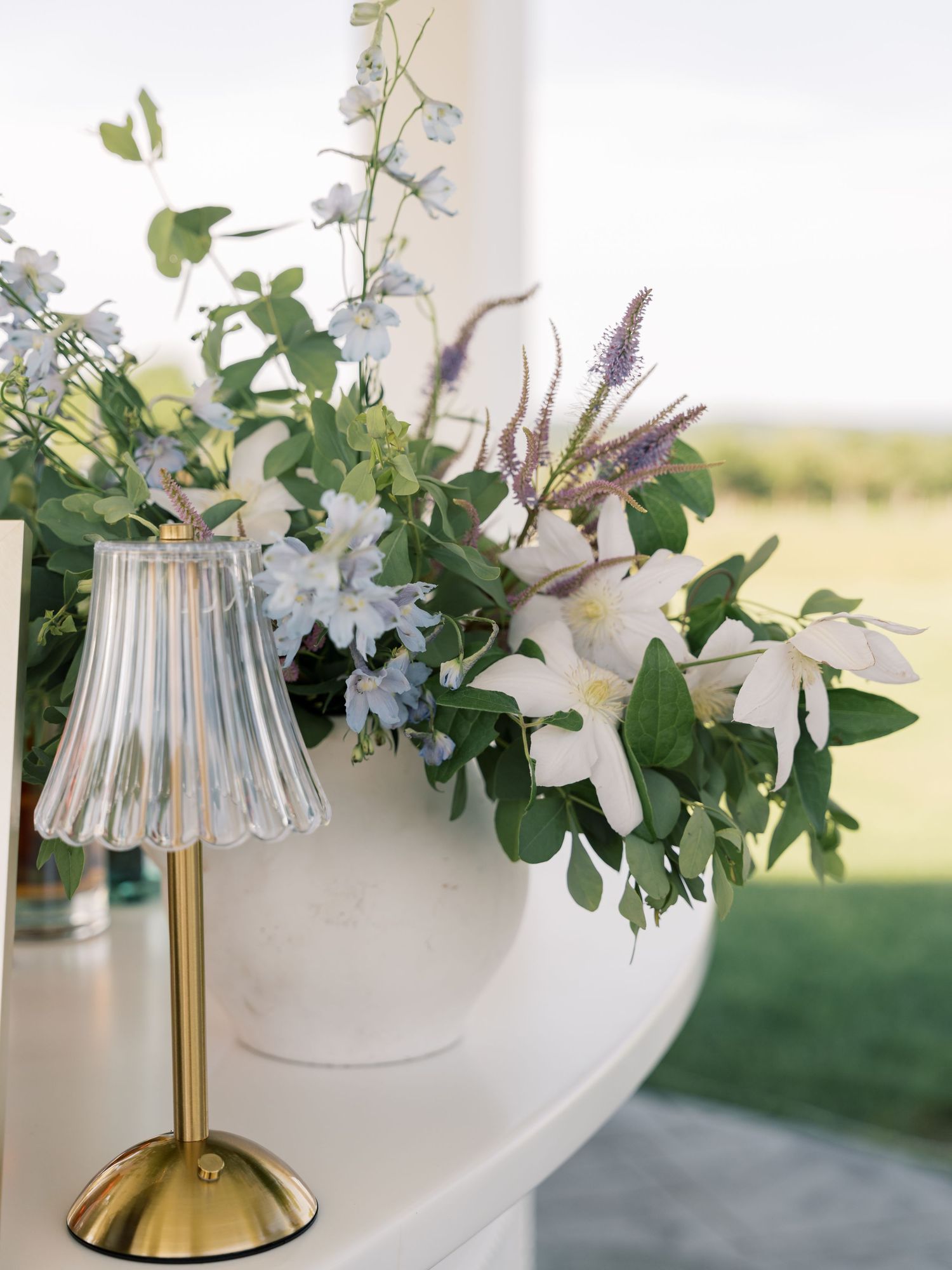 Modern table lamp with brass base and pleated glass shade decorated with elegant floral arrangements.