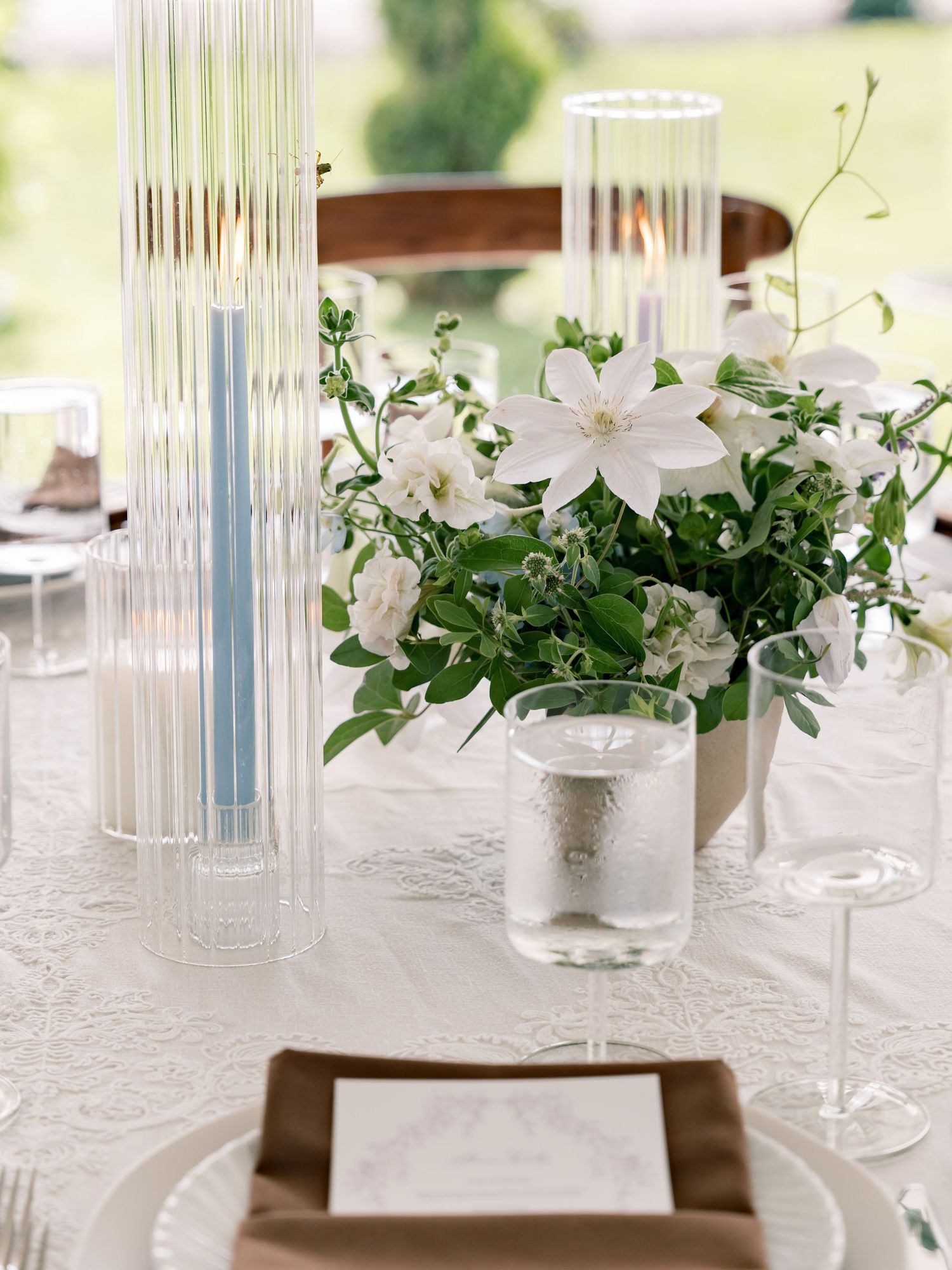 Elegant white floral centerpieces with lilies in glass vases on a white tablecloth at an upscale event setting.