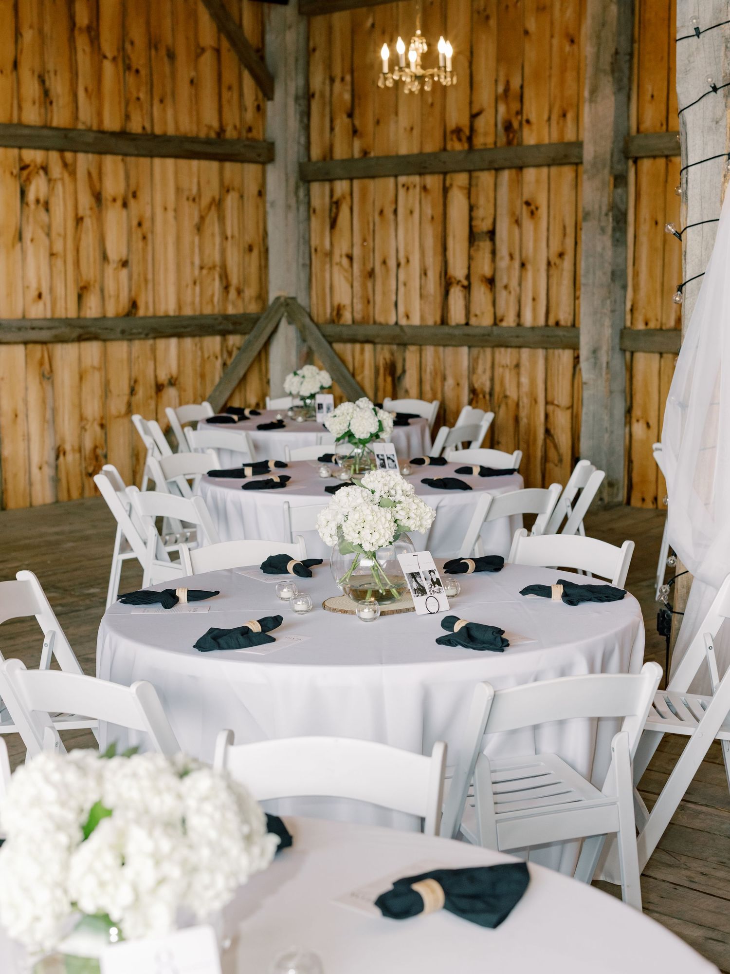 Elegant rustic barn wedding reception setup with round tables featuring white linens, navy napkins and hydrangea centerpieces.