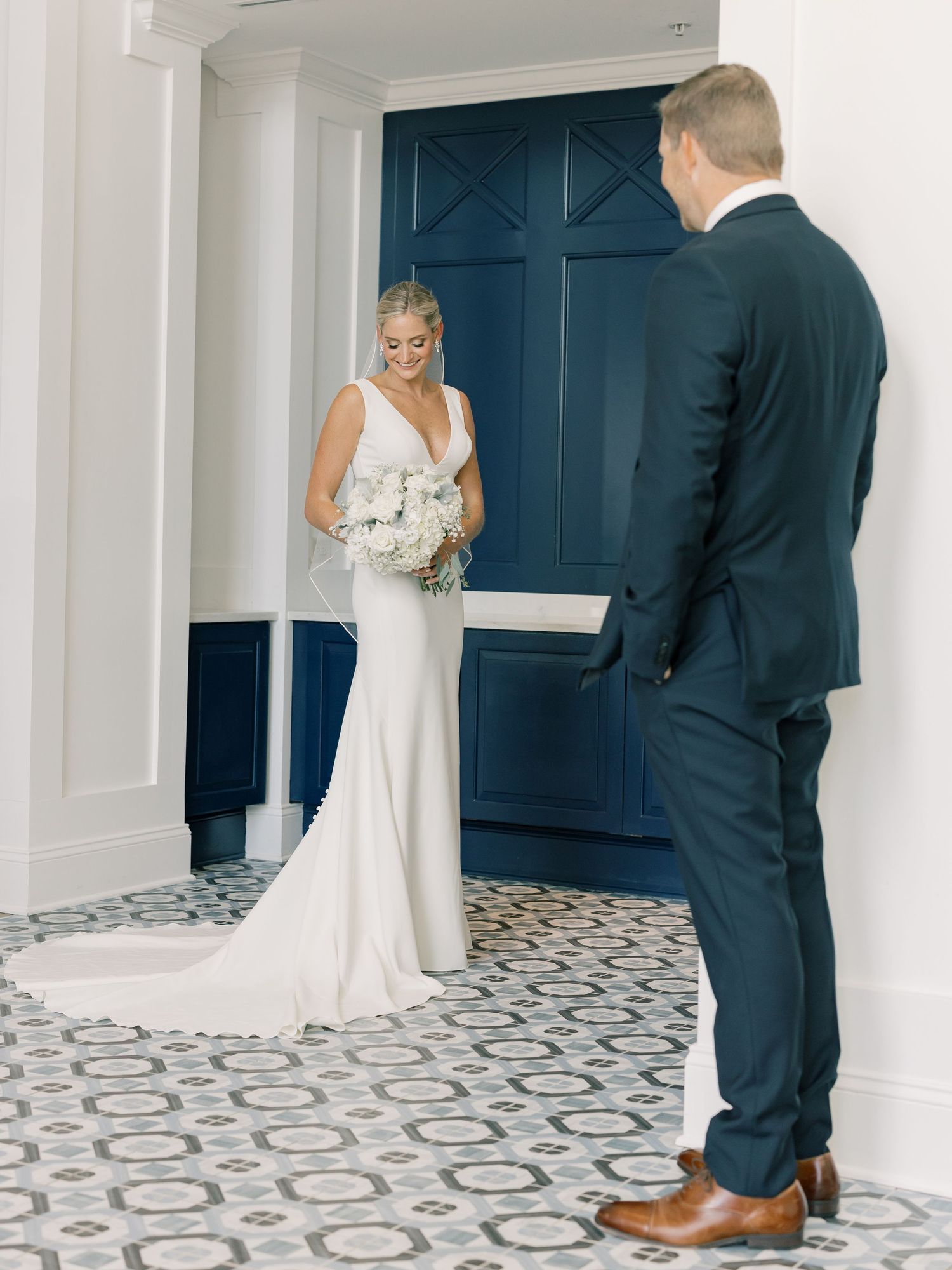 A couple shares their first look moment on patterned tile floors in an elegant white and navy venue setting.