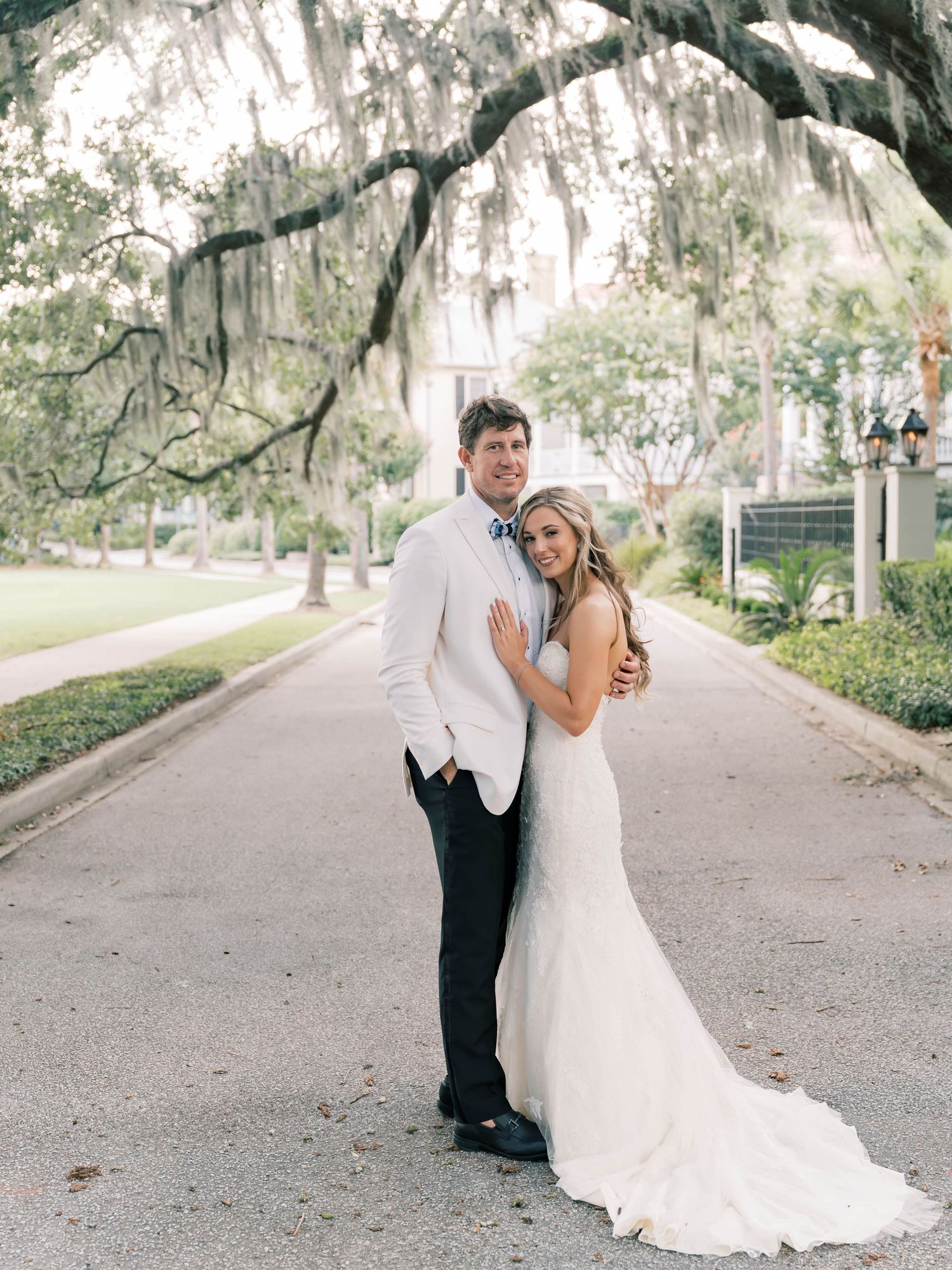 Wedding couple walking along a tree-lined path with Spanish moss hanging overhead.