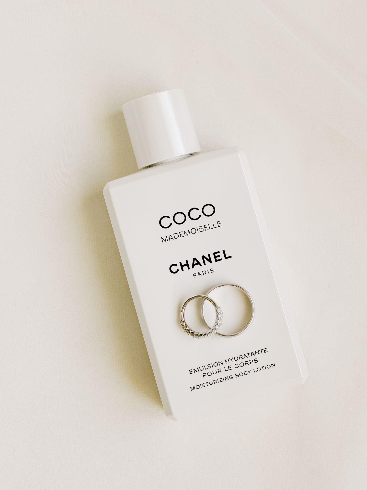 A minimalist arrangement of Chanel Coco Mademoiselle perfume bottles and delicate silver jewelry on a white surface.