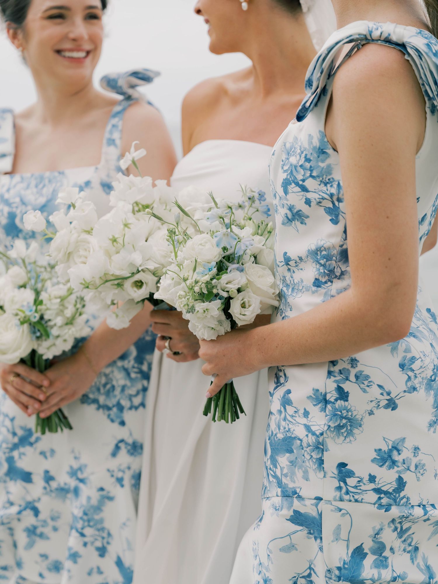 Bridesmaids in blue and white floral dresses holding white bouquets stand beside a bride in a white gown.