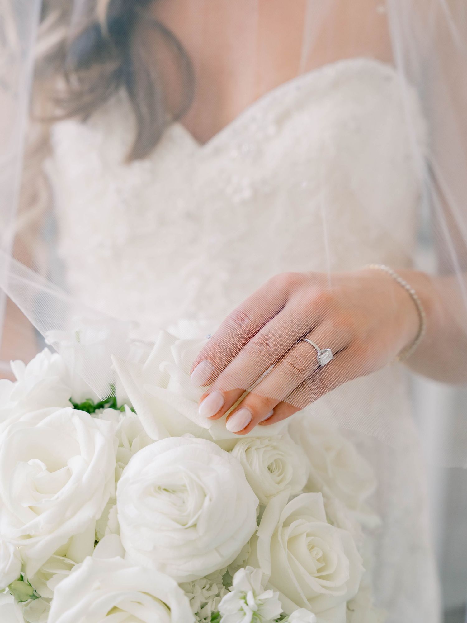 White roses and wedding bouquet details with diamond ring and lace veil.