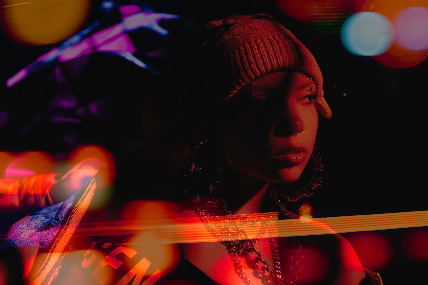 Artistic nighttime portrait with red and purple lighting effects showing figure wearing winter beanie in dark ambiance.