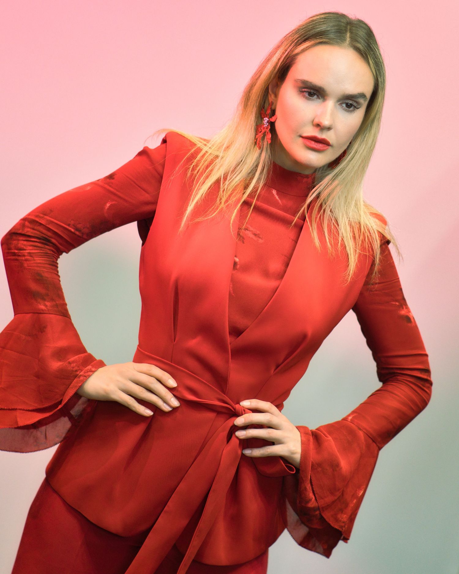 Fashion portrait series in vivid red featuring a fitted jacket with dramatic bell sleeves against a pastel backdrop.