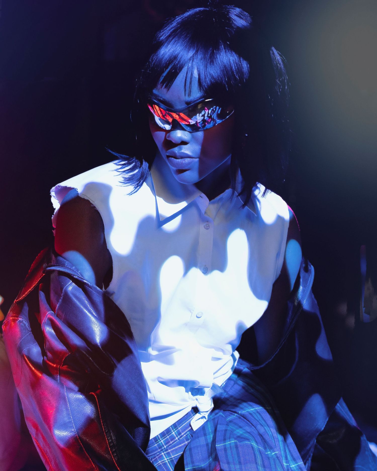 Figure in white top and red sunglasses poses dramatically against dark background with atmospheric lighting effects.