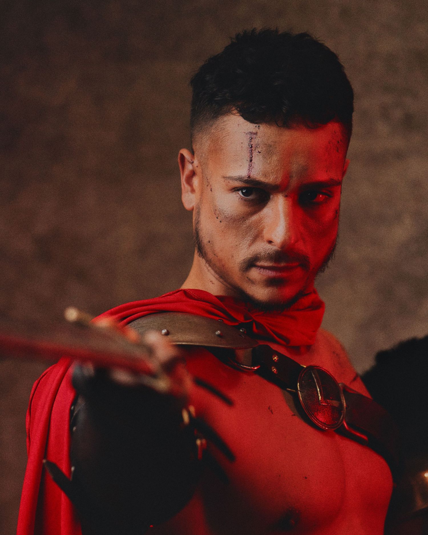 Dramatic portrait in red lighting shows person wearing red clothing while holding violin against dark background.