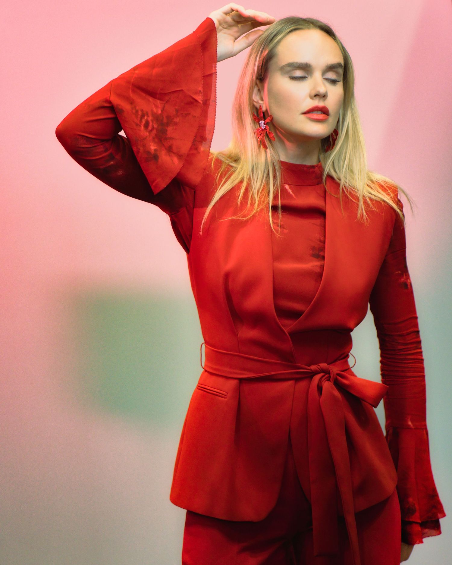 Fashion model in vibrant red monochromatic outfit with blazer and matching dress against pink background.