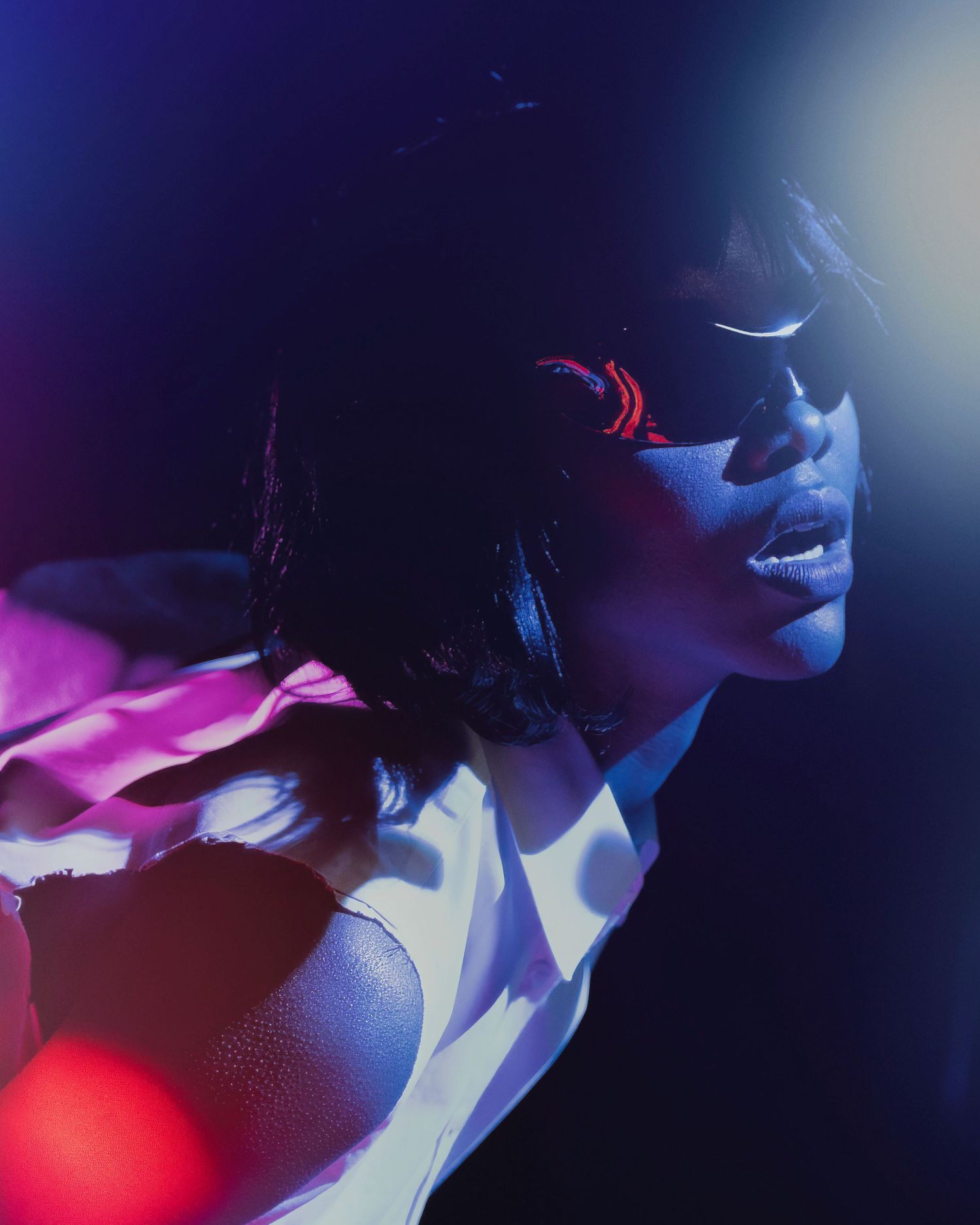 A person poses in dramatic lighting with pink and blue hues creating a moody artistic portrait.