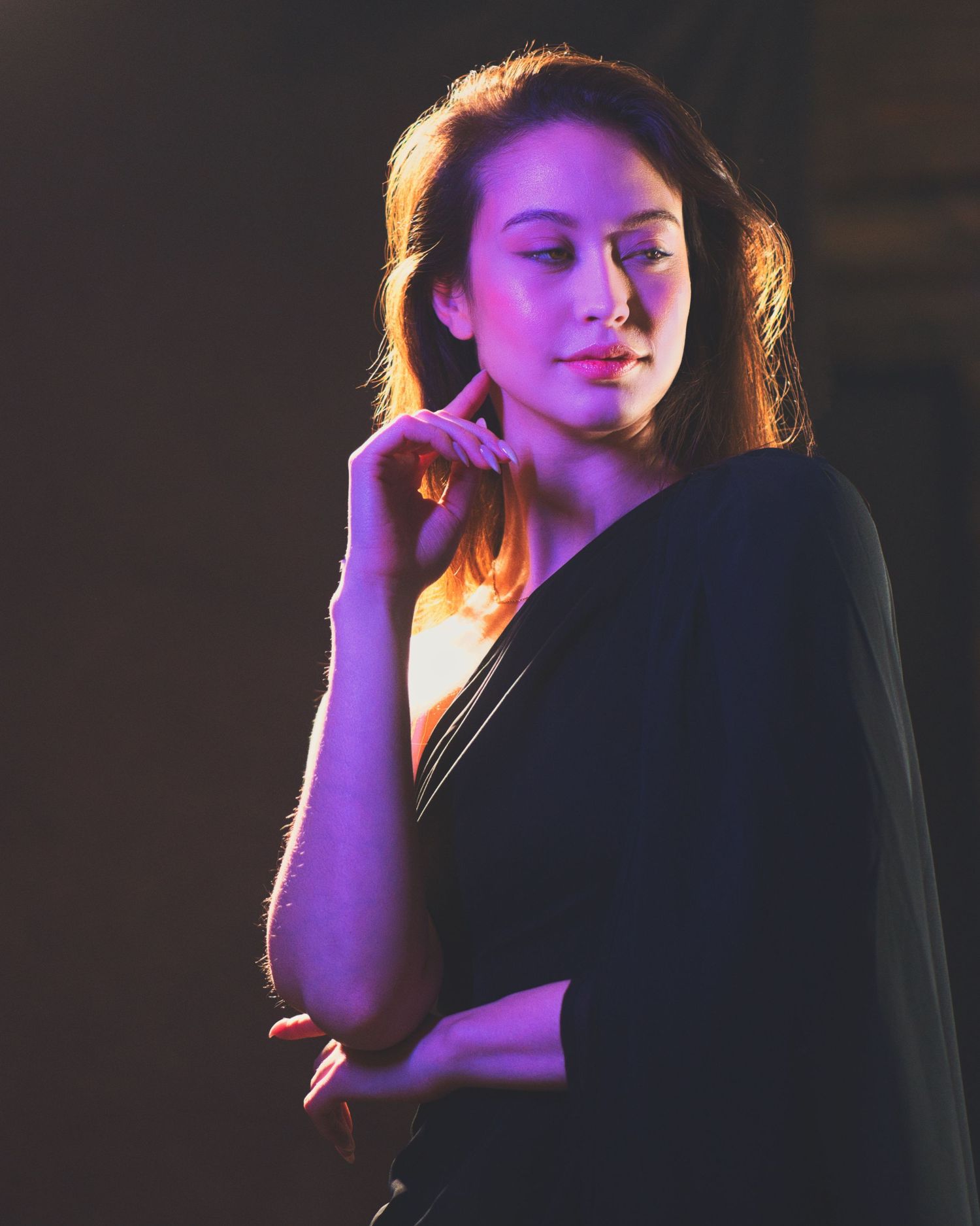 Artistic portrait in moody lighting with purple and orange tones showing contemplative pose against dark background.