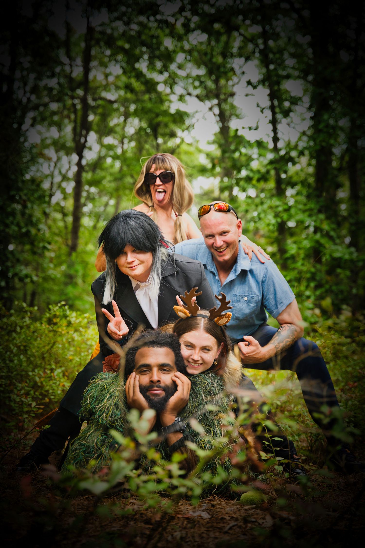 A group of friends peek out playfully from behind greenery in a forest setting.