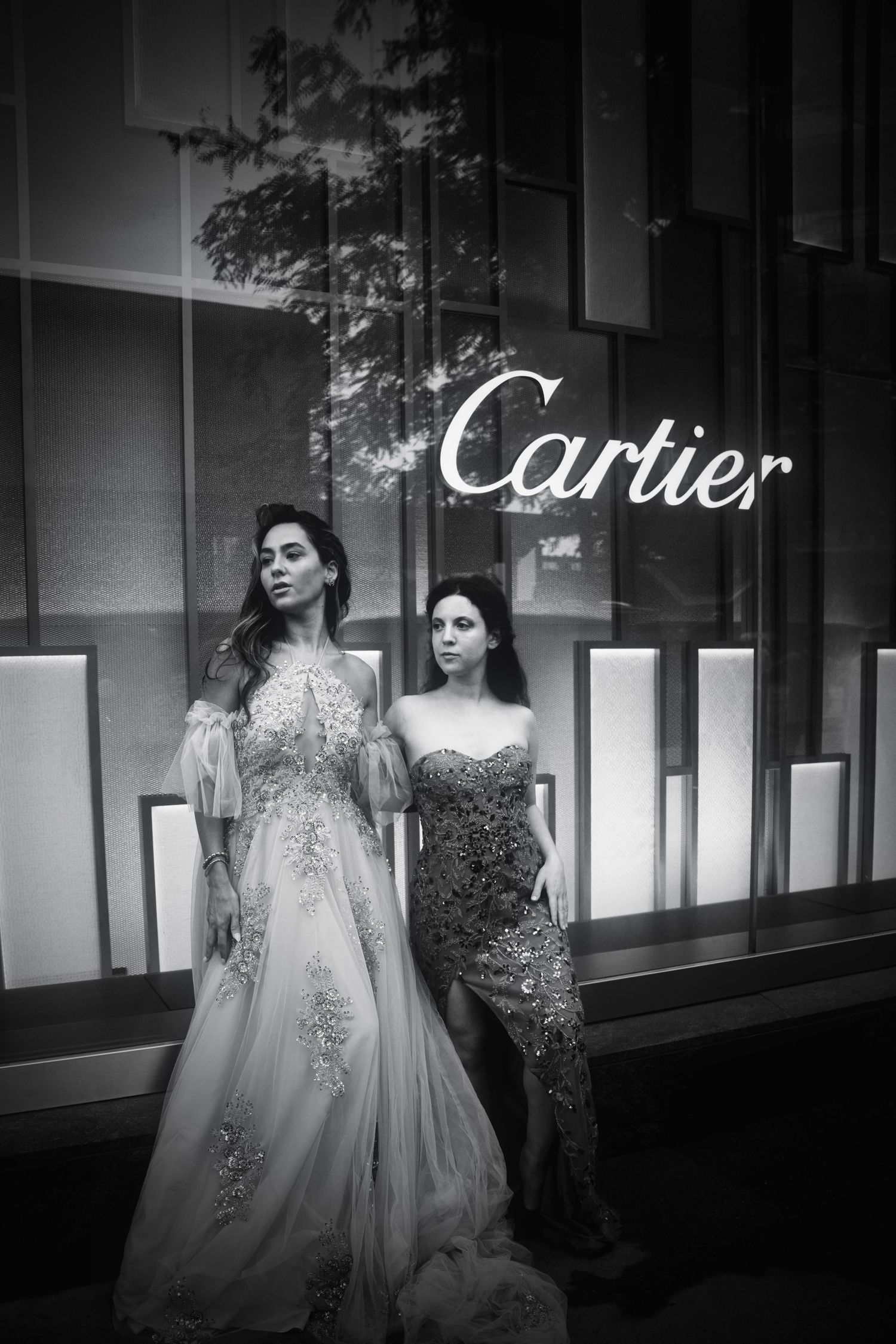 Black and white fashion photograph showing elegant gowns outside illuminated Cartier storefront.