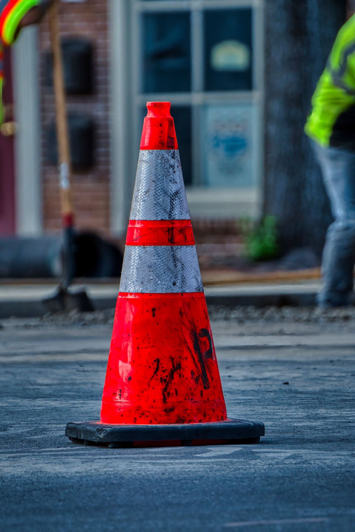 Four red and black traffic cones arranged in a row on urban pavement with blurred background.