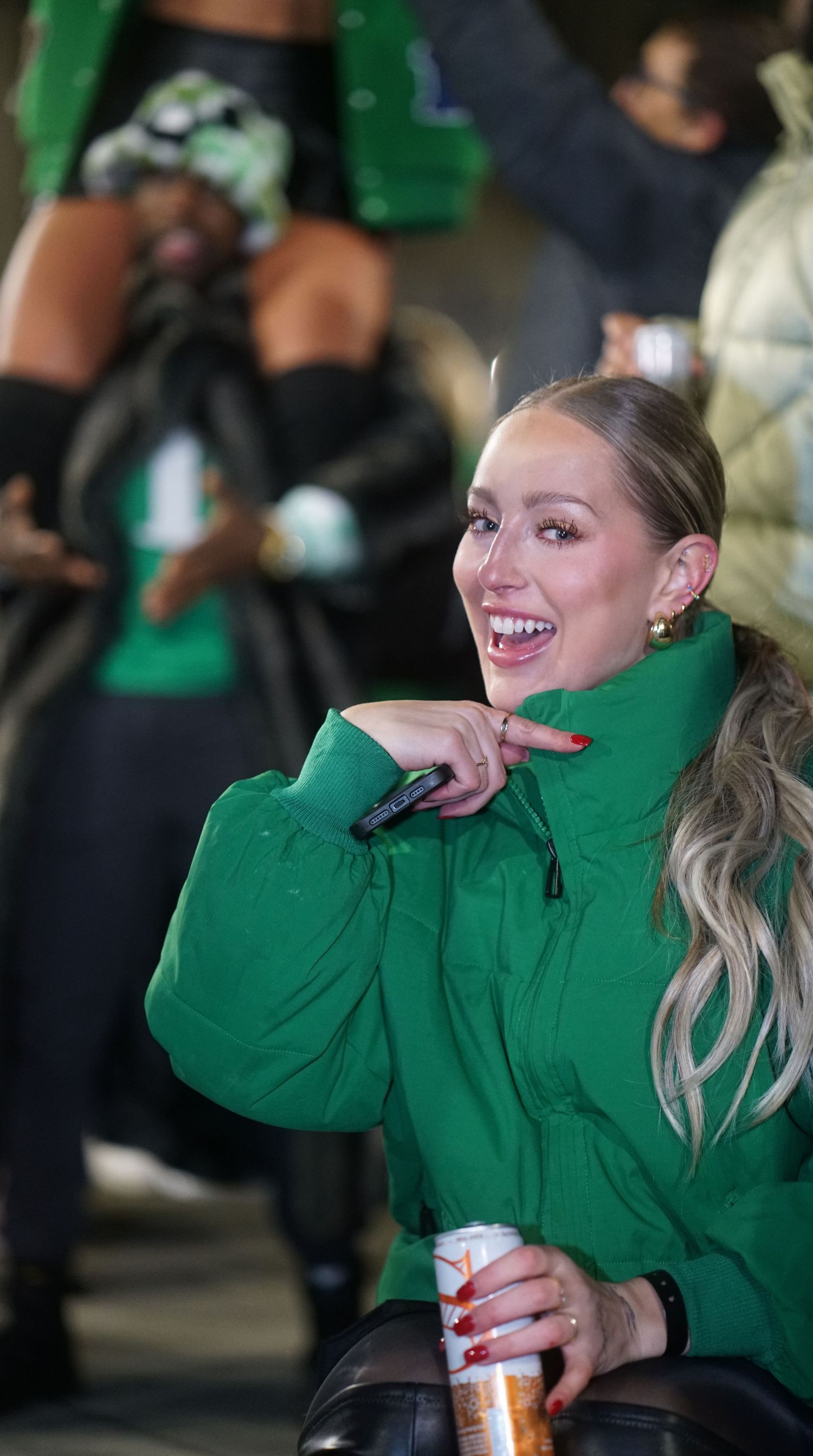 A person in a bright green turtleneck sweater smiles while holding a drink can at an event.