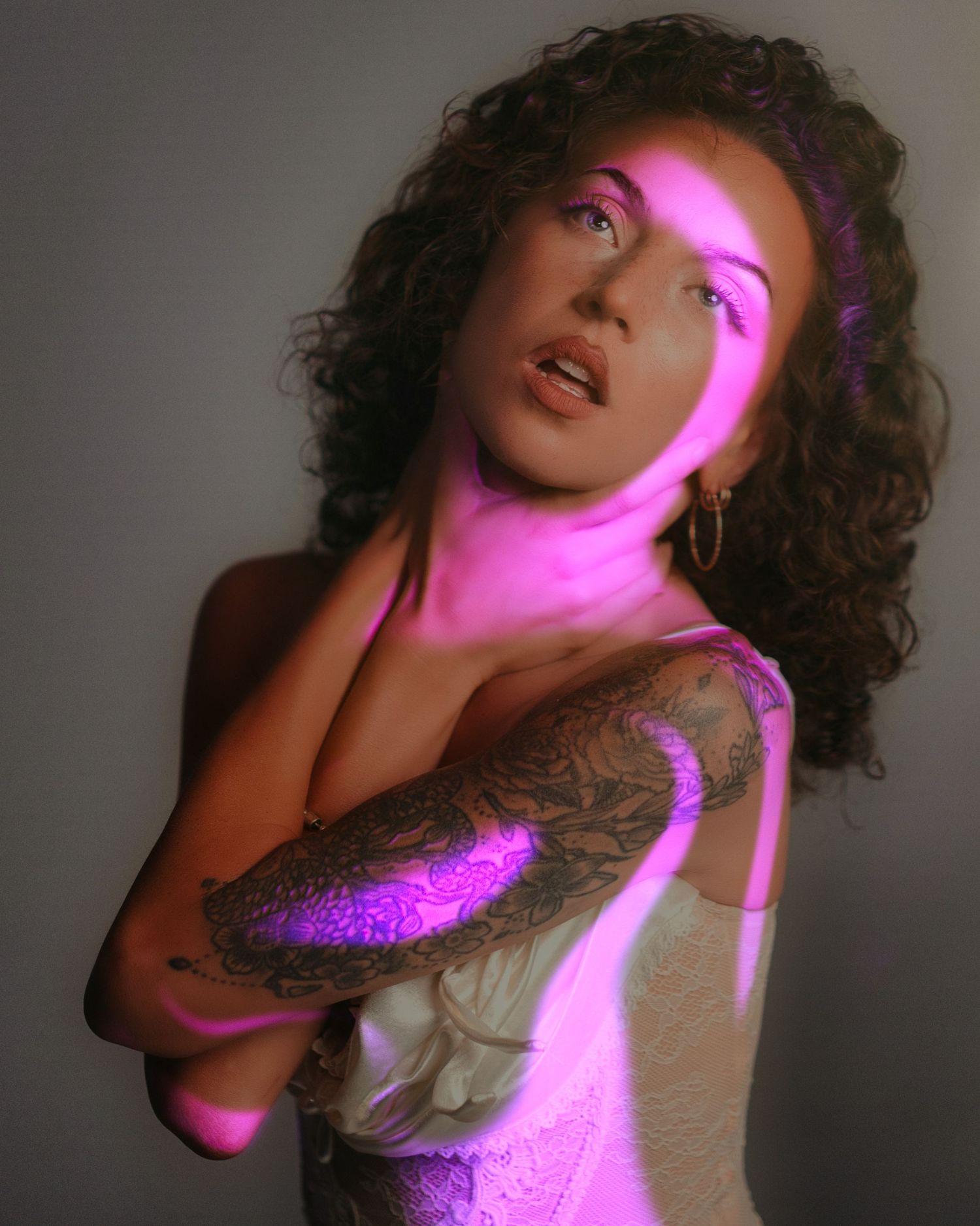 Artistic portrait with neon pink light effects casting dramatic shadows on a person with curly hair against neutral backdrop.