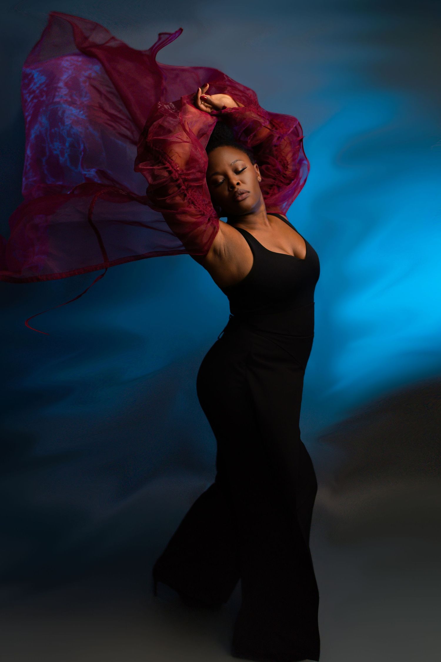 A dancer in a black dress moves gracefully against a dark blue background as red fabric flows through the air.