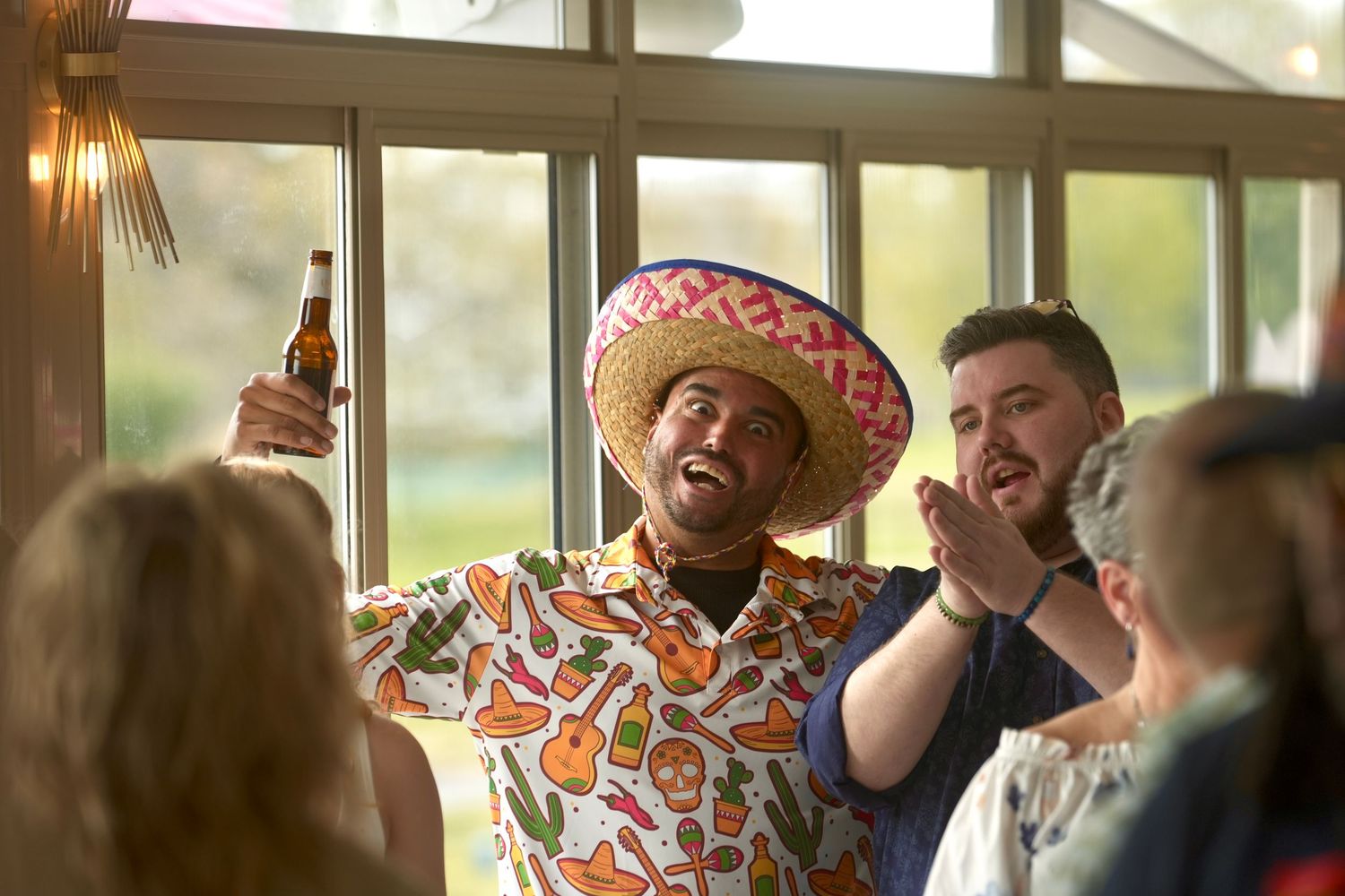 A group of people in colorful attire celebrate and laugh together in a sunlit room during a festive gathering.