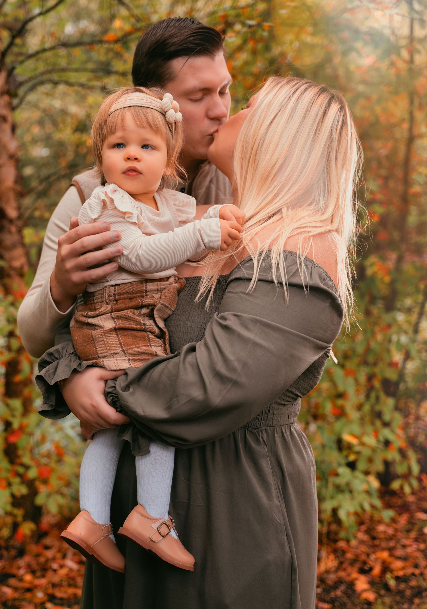 A family shares tender moments together during an autumn photoshoot with fallen leaves and warm colors in the background.