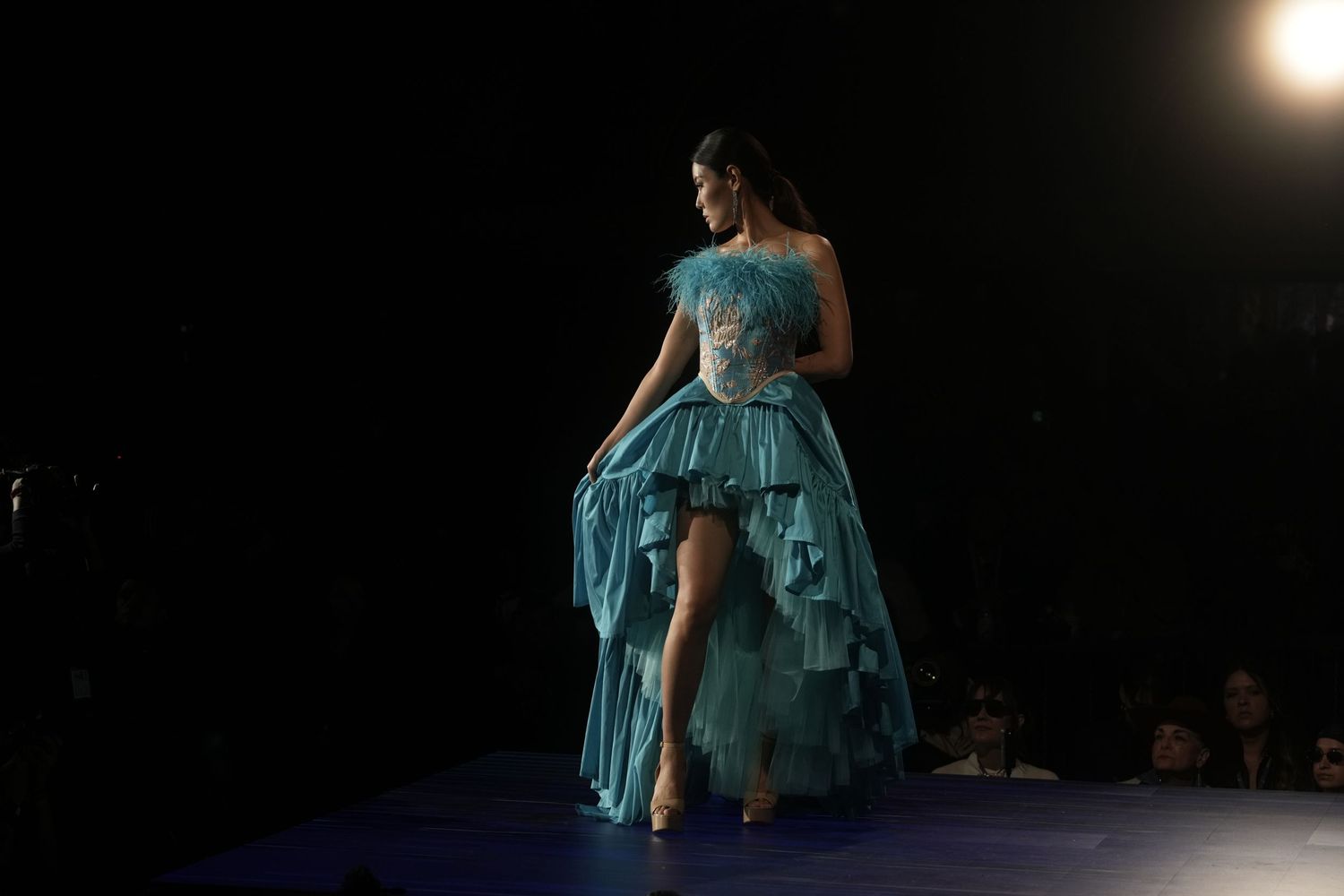Dancers in flowing blue dresses perform a contemporary dance piece on a dark stage illuminated by spotlights.