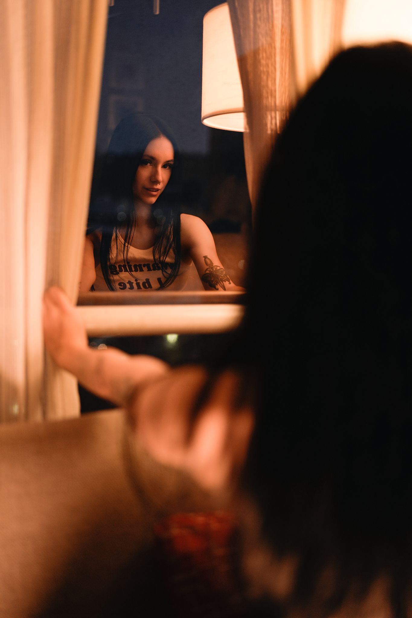 A dark and moody portrait photo taken through a window with warm lighting creating a reflective atmosphere.