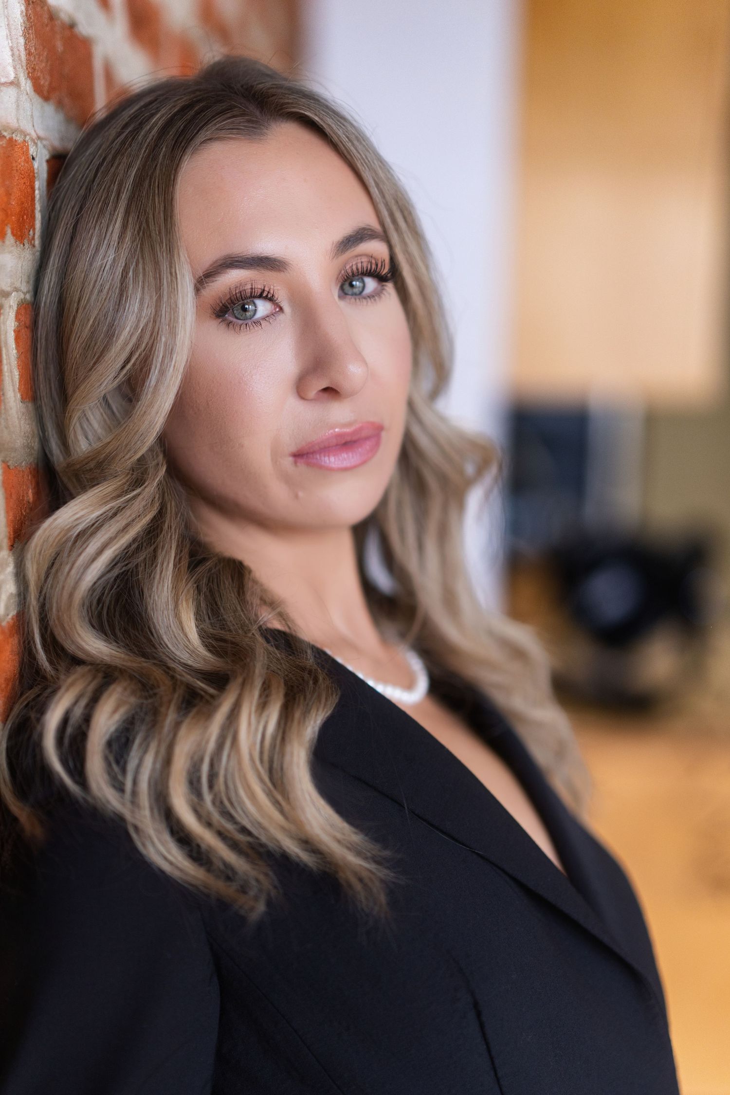 Professional headshot series showing a woman in a black blazer with wavy blonde hair against a warm-toned background.