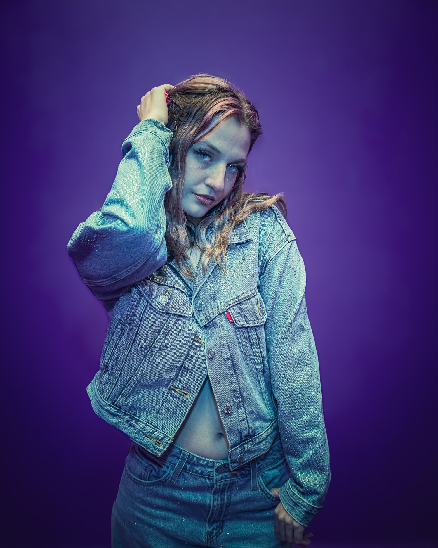 A figure in a denim jacket poses against a purple backdrop in a stylized fashion photoshoot series.