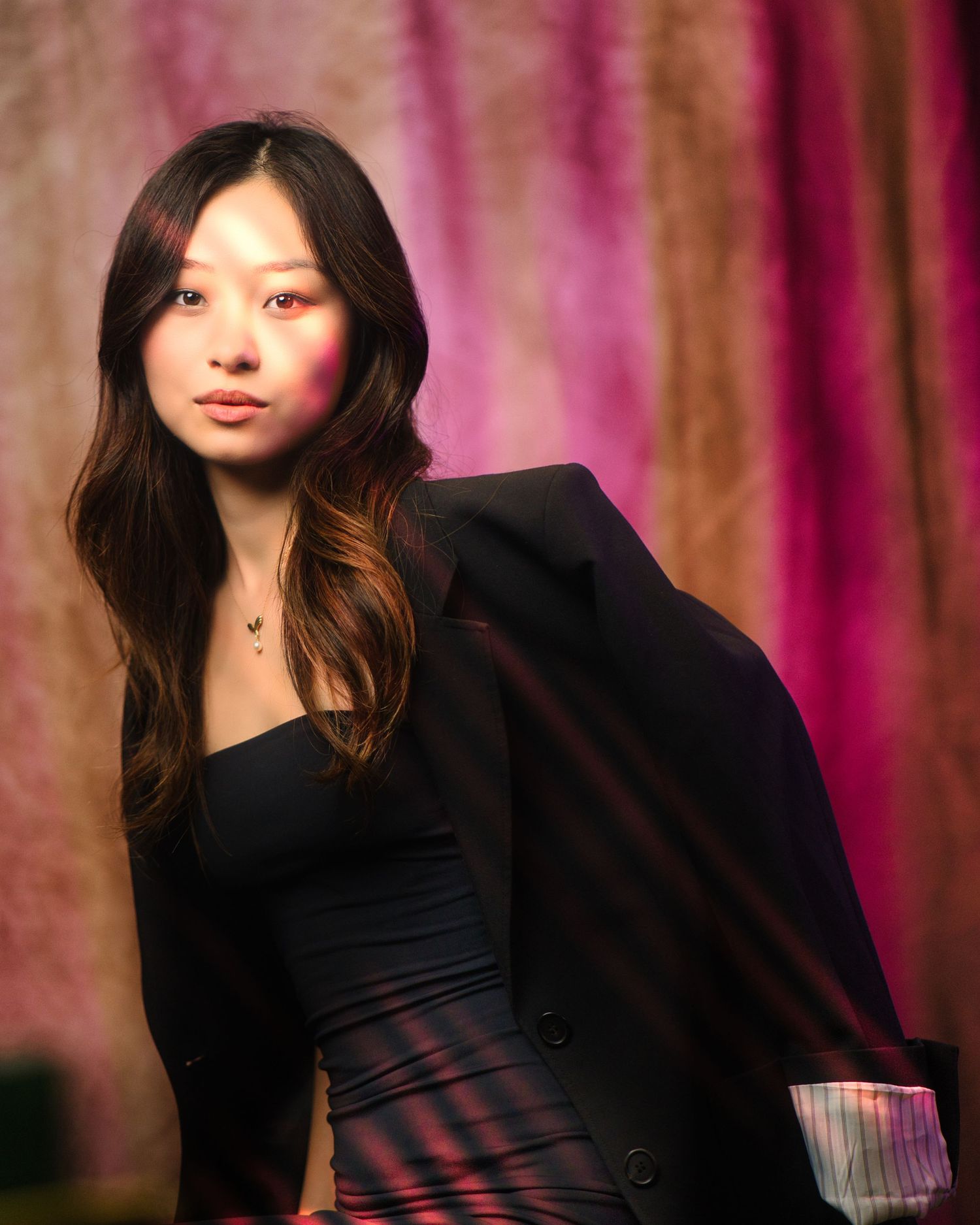 A fashion portrait series featuring dark-haired model in black against a colorful purple and pink draped backdrop.