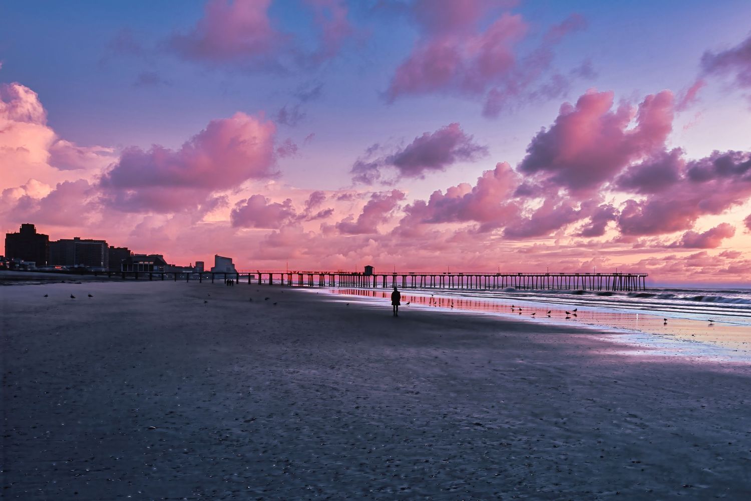 Stunning pink and purple sunset sky over Myrtle Beach pier with silhouetted buildings along the dark shoreline.