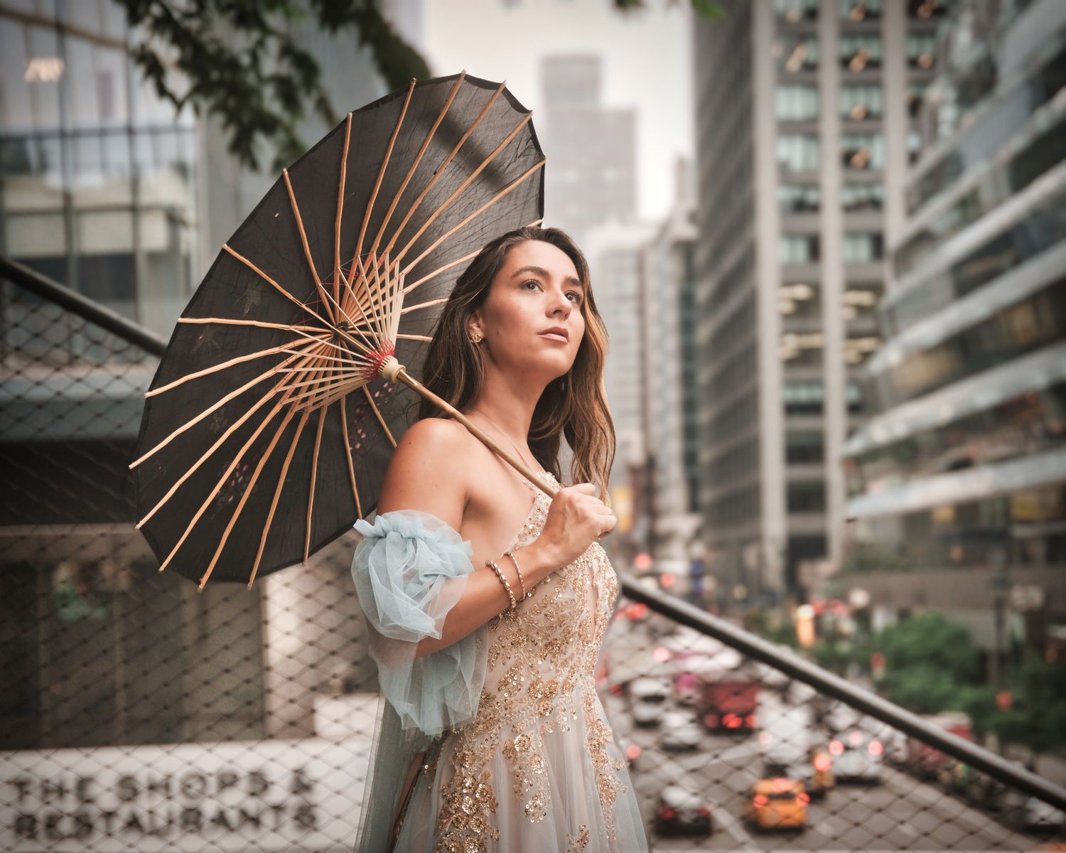 Elegant figure poses with vintage parasol against urban cityscape backdrop with tall buildings and street traffic below.