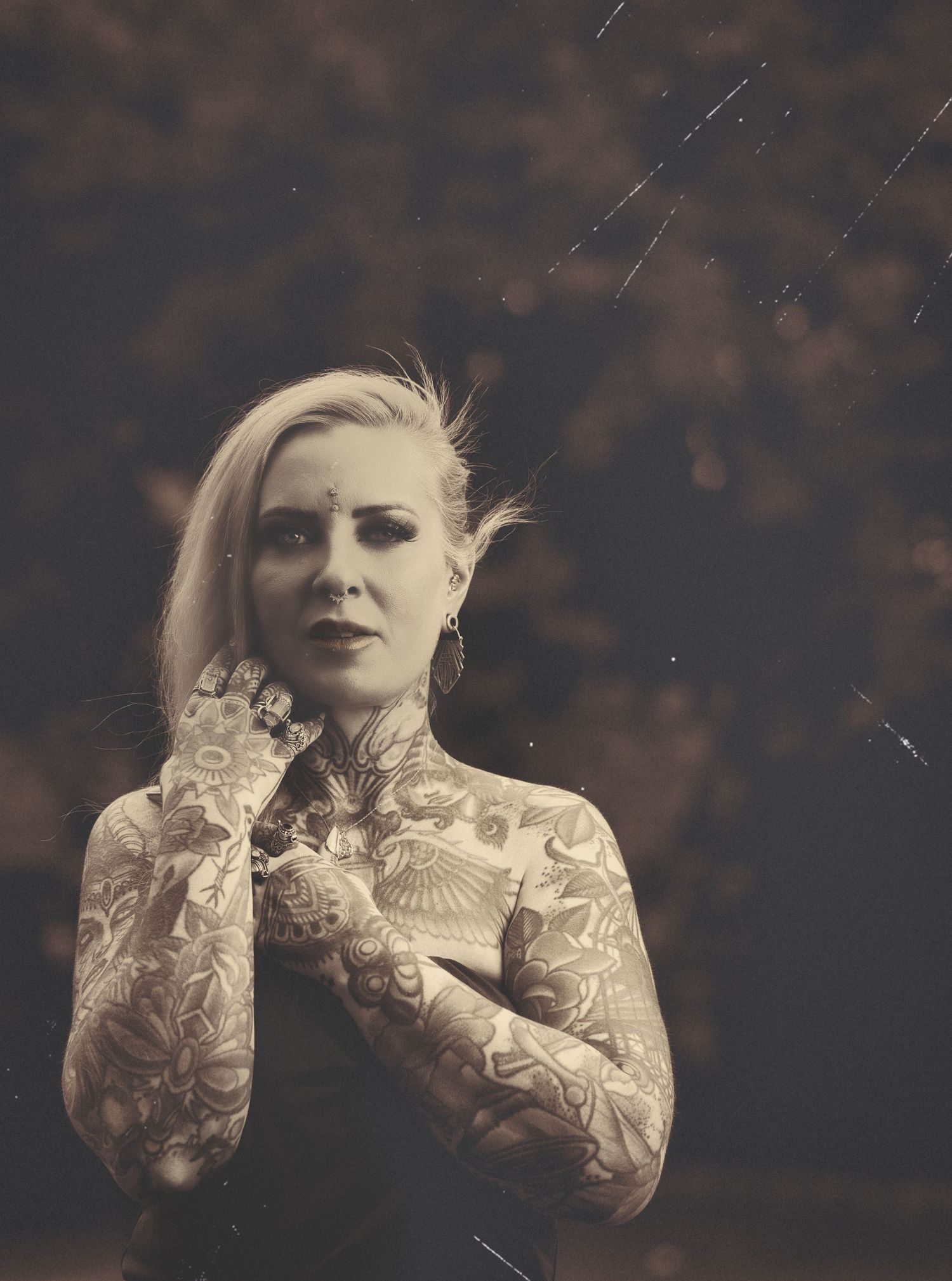 Artistic black and white portrait showing heavily tattooed arms in elegant dramatic pose against dark background.