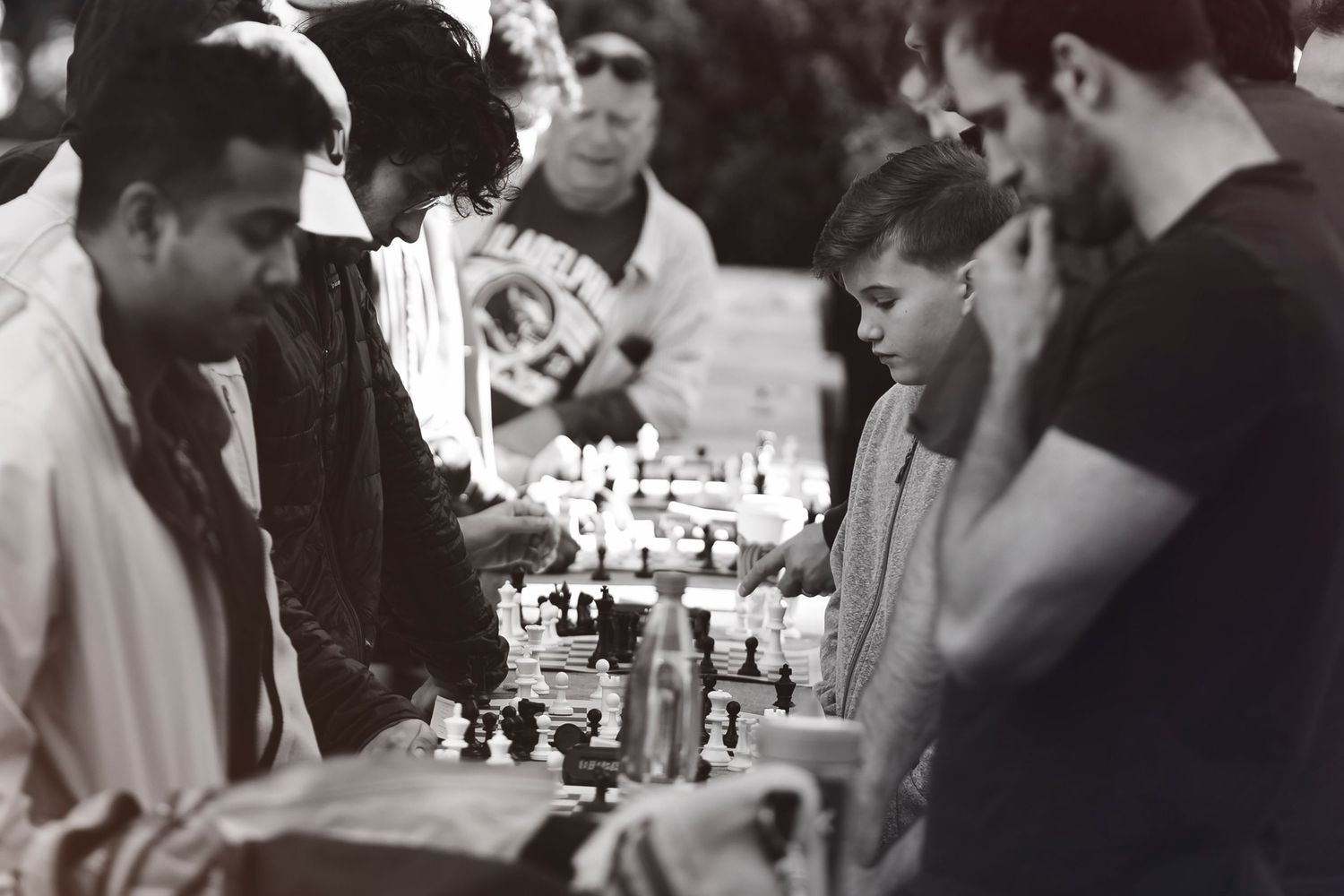Black and white photograph of people intensely focused around a chess game in what appears to be a casual setting.