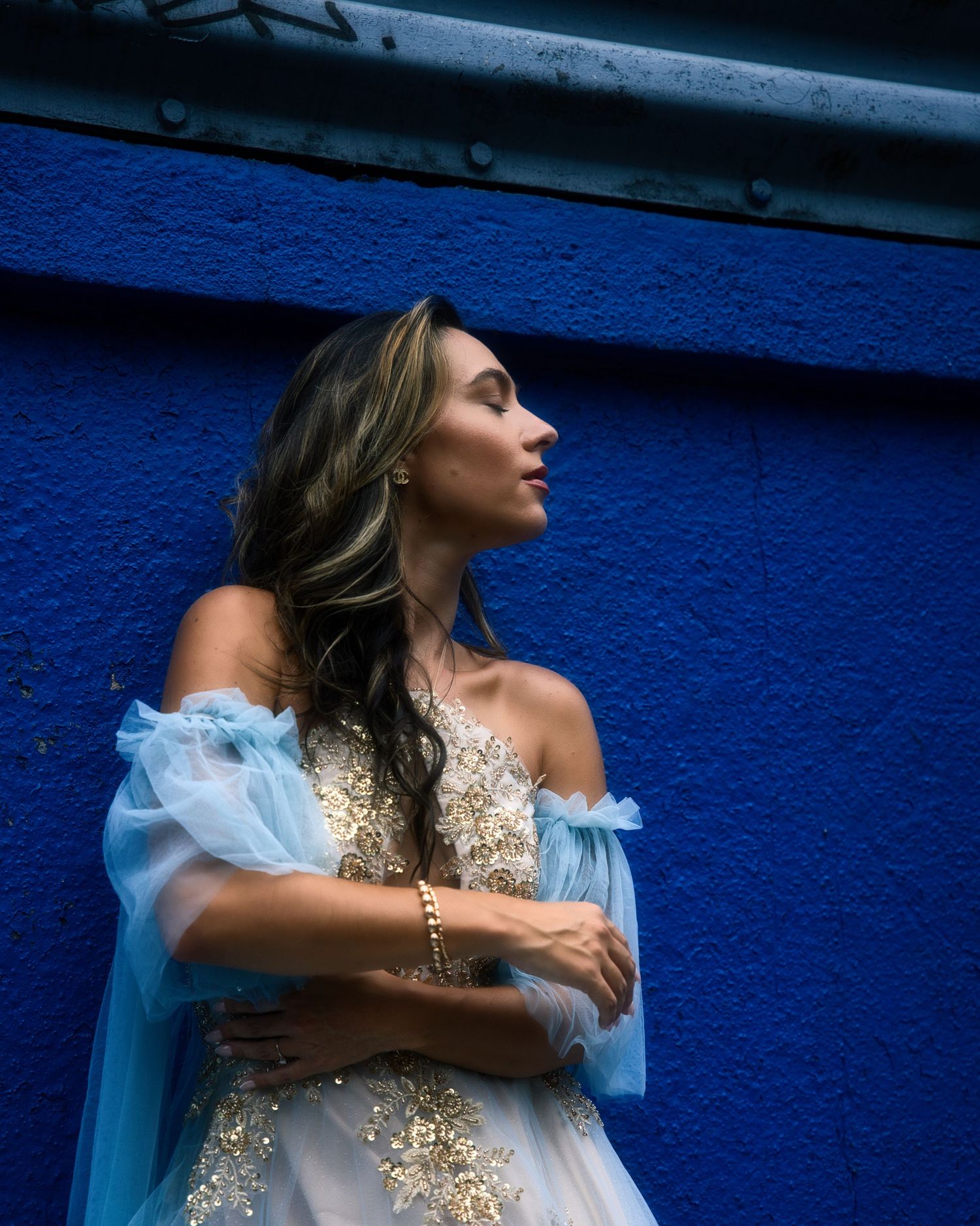 Fashion portrait with delicate light blue and gold dress against vibrant cobalt blue wall setting.