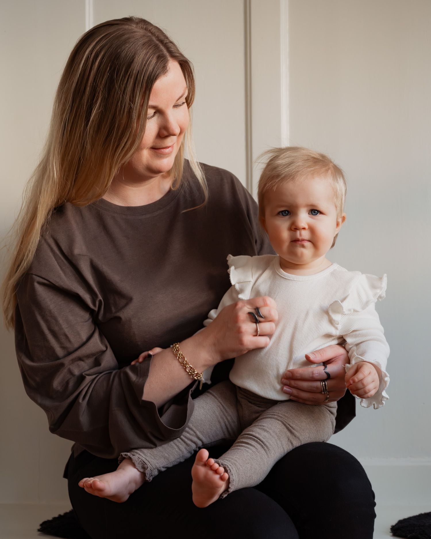 Parent and baby in matching brown and white outfits pose together against neutral wall in candid photo series.