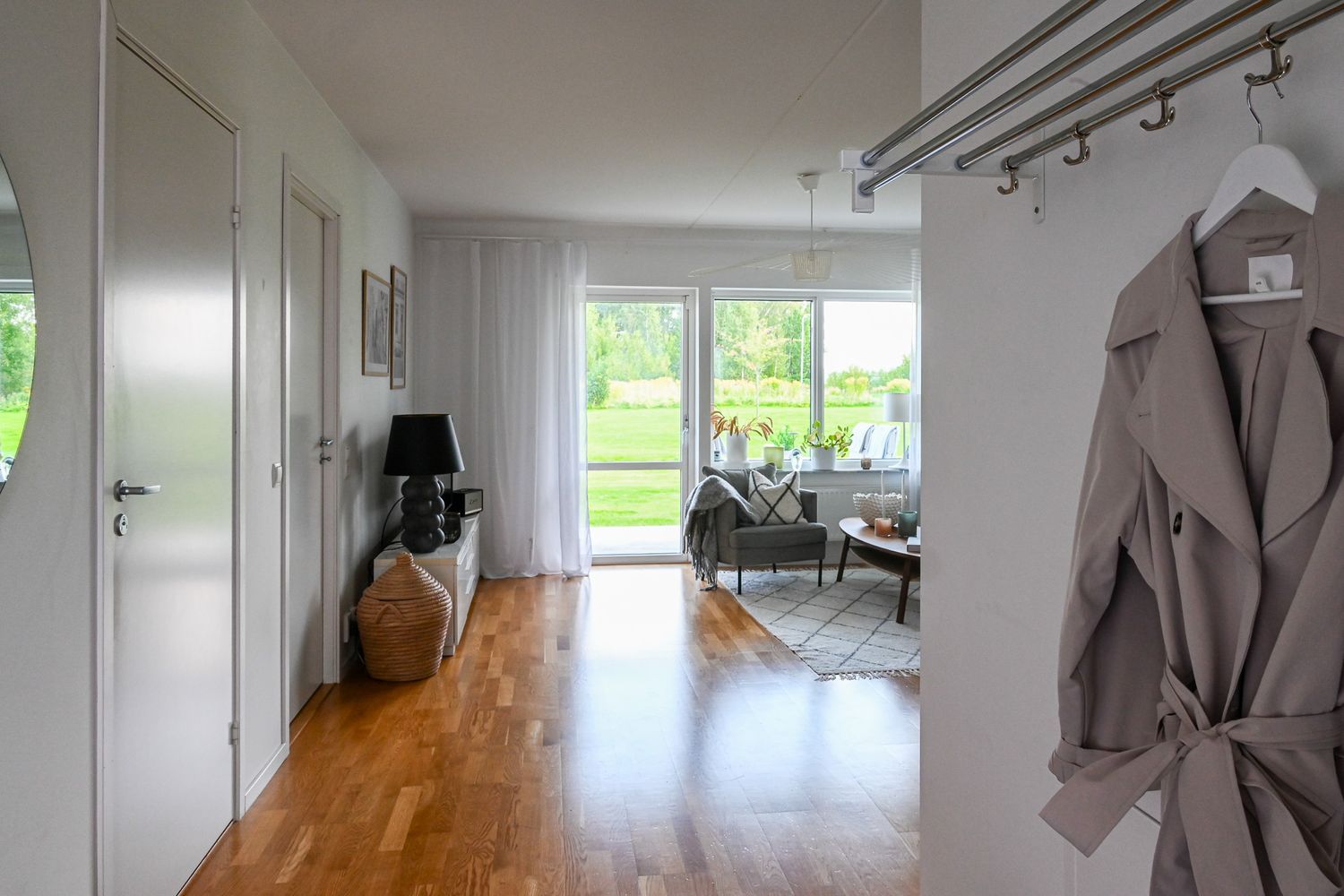 Bostadsfoto entré med jacka som hänger prydligt och genomgående öppen planlösning in till vardagsrum med utgång till solig altan.