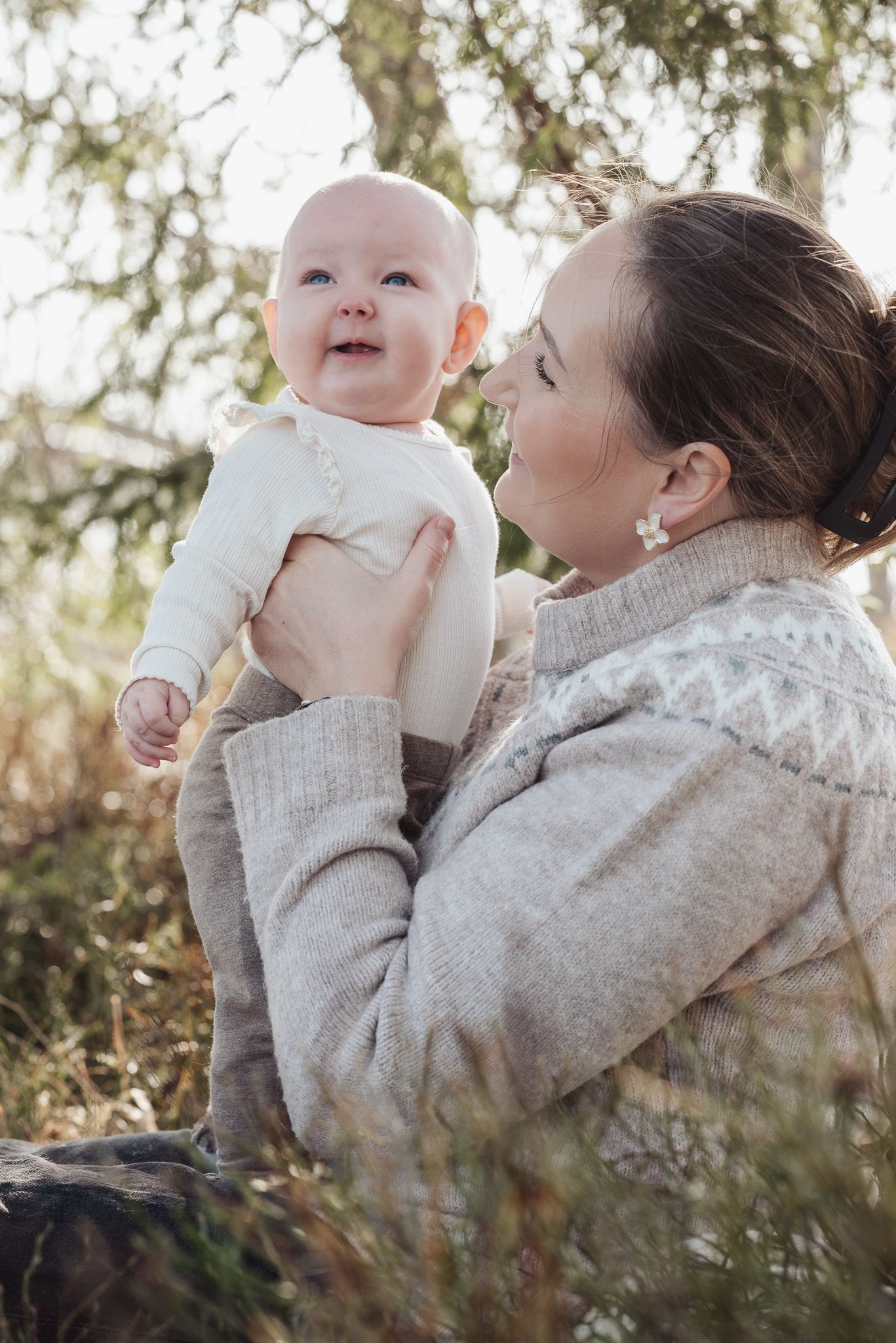 A tender moment between parent and baby in matching gray sweaters captured in a series of outdoor portrait photos.