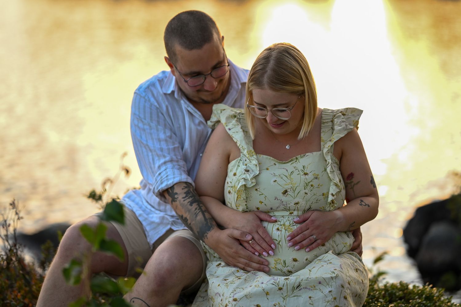 Romantiskt par håller om varandra och gravidmagen under golden hour fotosession gravidfotografering.