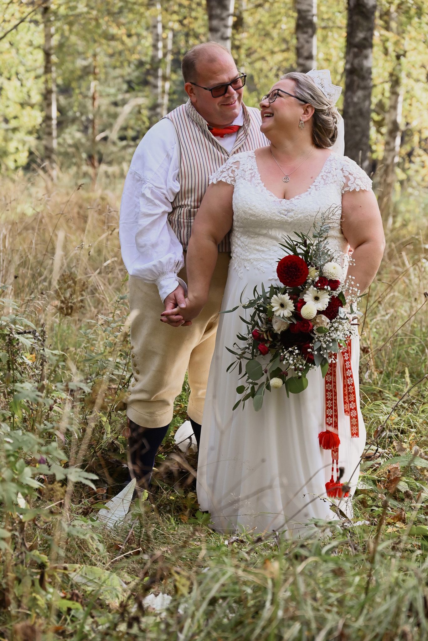 Romantiskt bröllopsporträtt taget utomhus i björkdunge där bruden håller bukett och paret ser på varandra med kärlek.