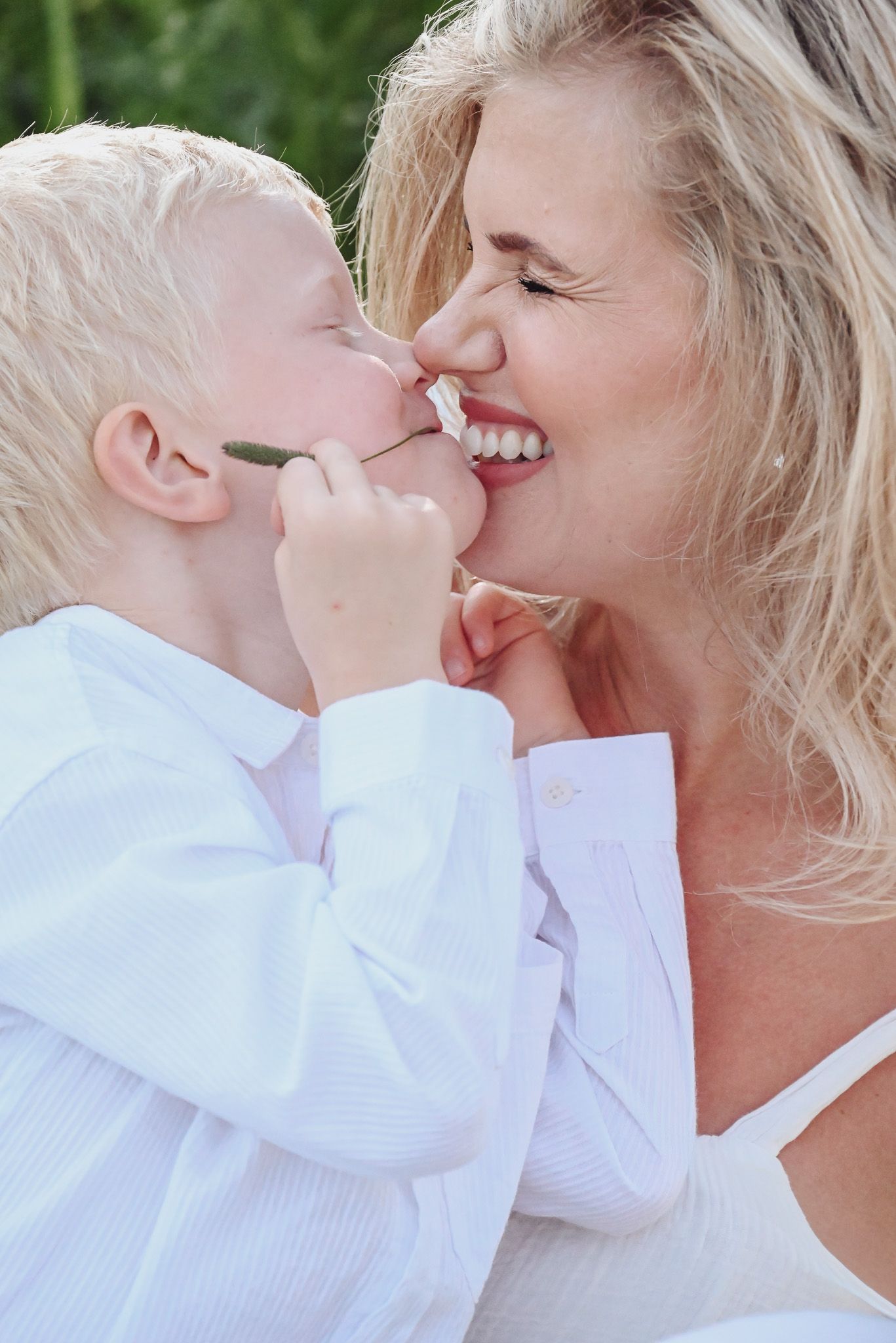 A tender moment of shared joy and laughter between a young child and adult wearing white against a green outdoor background.