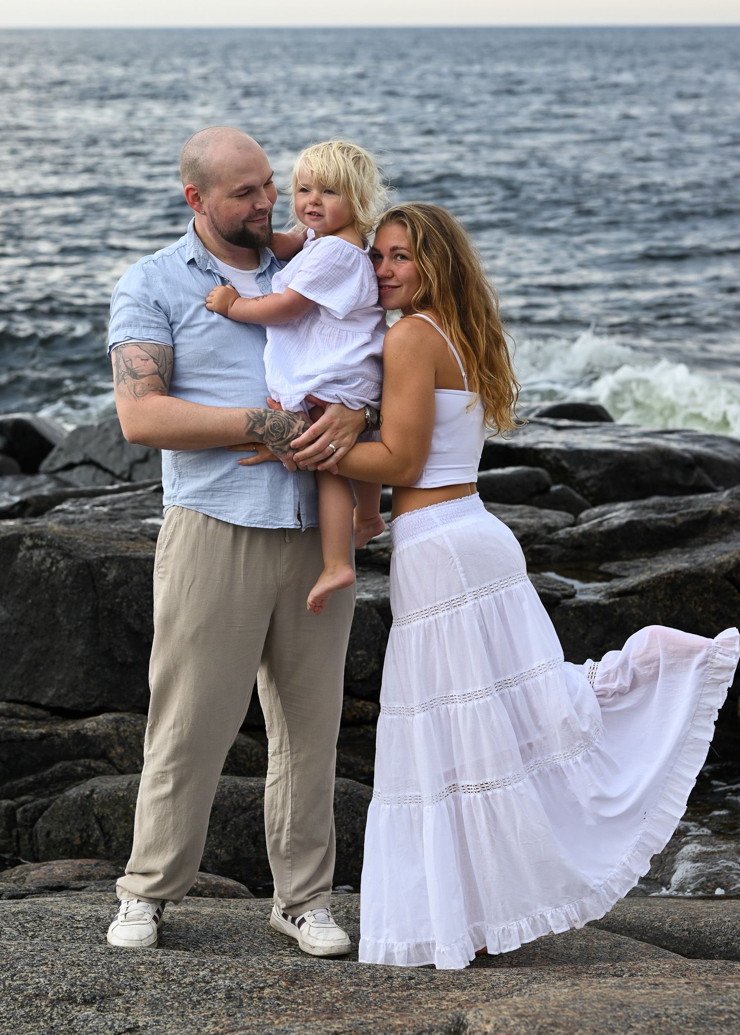 Romantiskt par med deras dotter vid havet under familjefotografering.