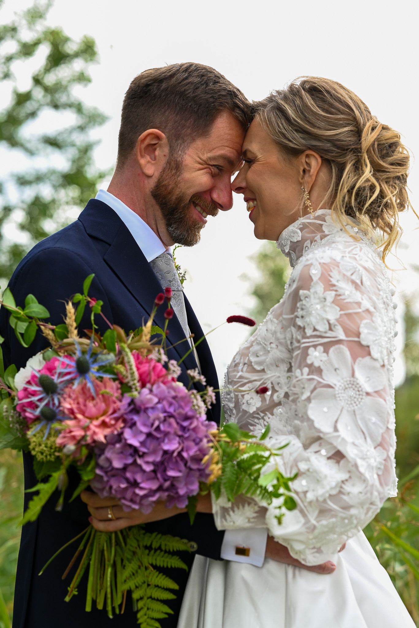 Brudpar delar ett romantiskt ögonblick medan de håller i en färgglad brudbukett med lila och rosa blommor.