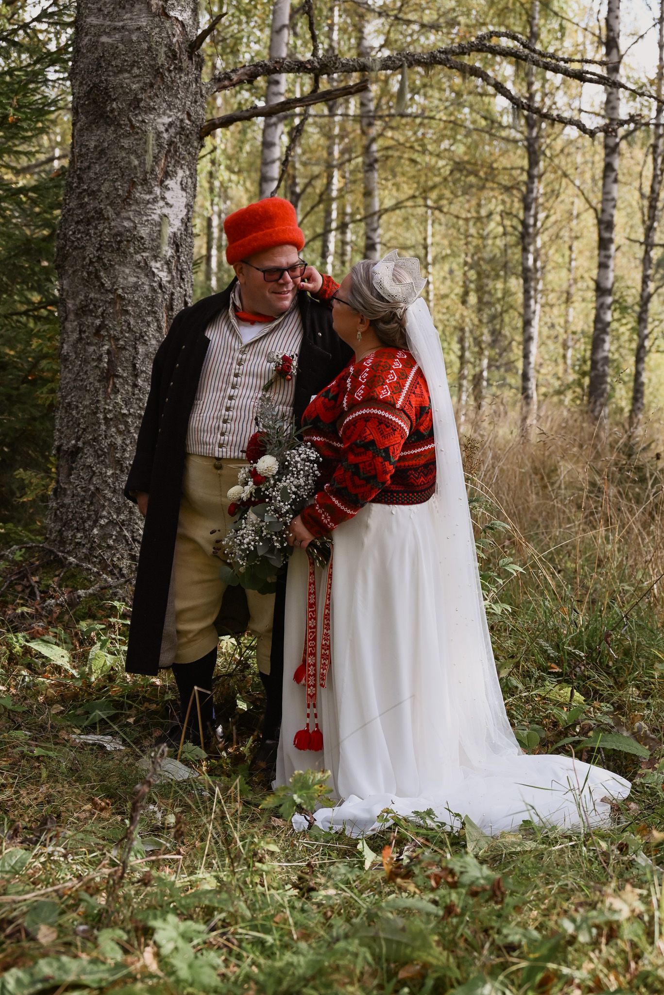 Bröllopsfoto på brudpar i folkdräkt från Delsbo och Norge taget utomhus med grönskande bakgrund.